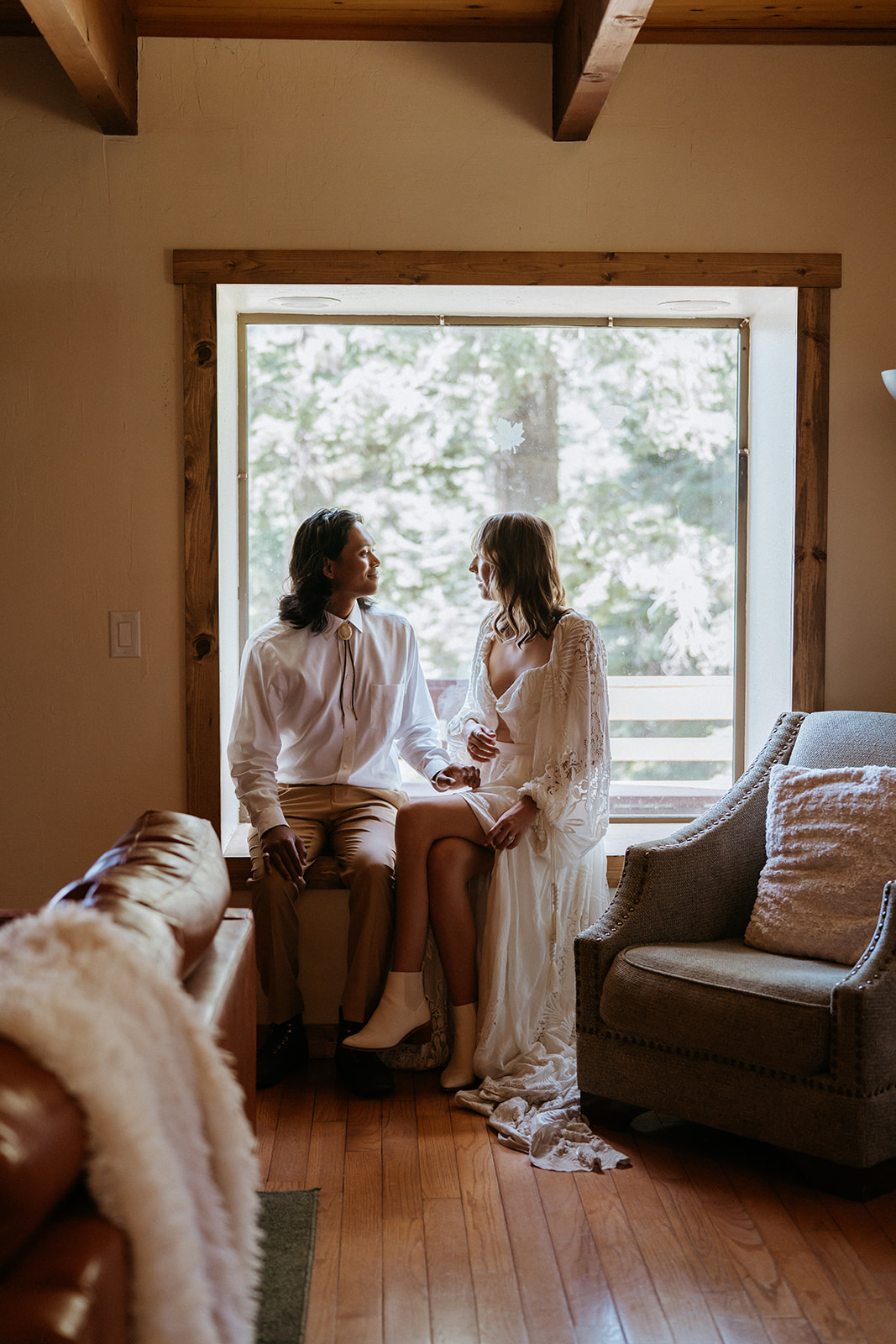 Newlyweds sit in a window together in a lace dress and tan suit