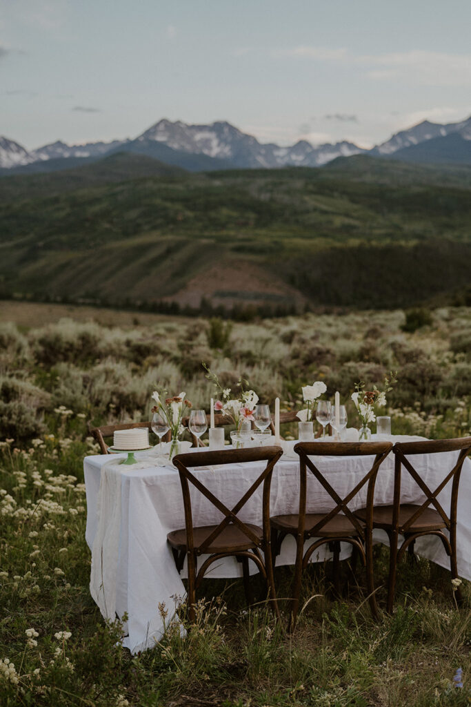 A private tablescape set in the Breckenridge mountains, decorated with white linens, florals, candles, and a small cake.