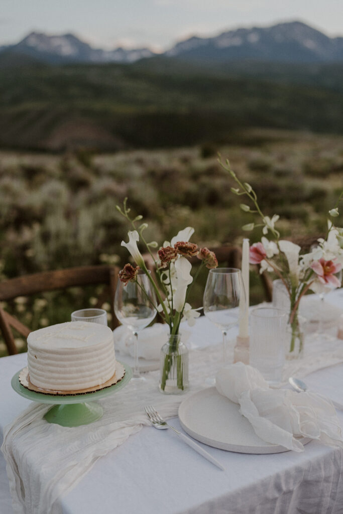 Close-up of the elopement table with floral bud vases, candles, and a white cake on a green stand against the mountain backdrop.