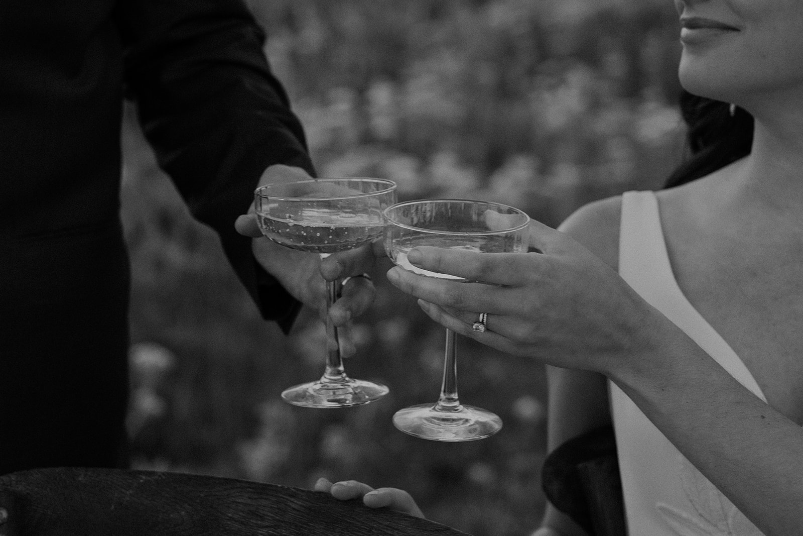 Black and white photo of the couple clinking coupe glasses filled with champagne.