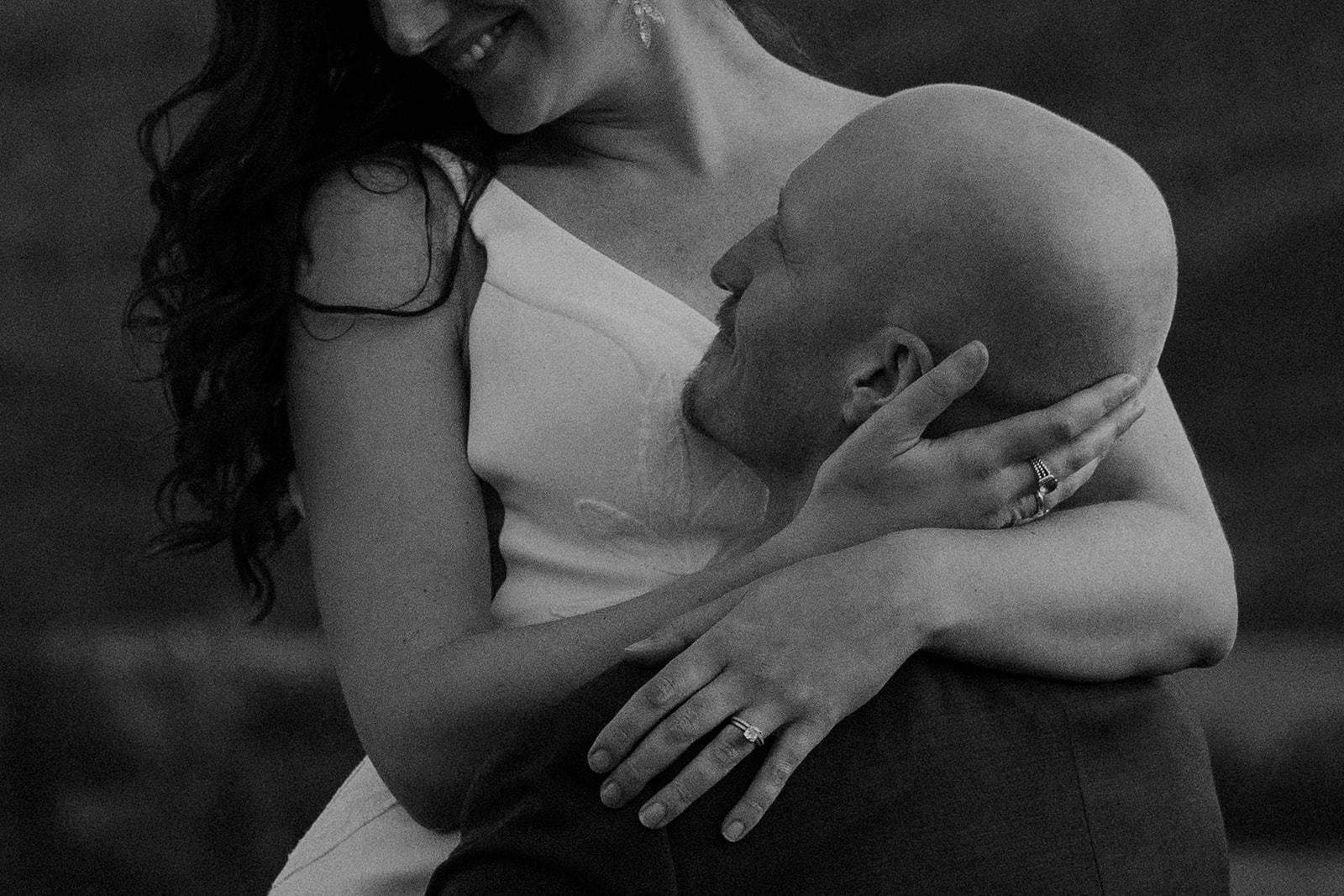 Black and white close-up of the bride smiling while holding her groom’s face, showing her wedding ring.