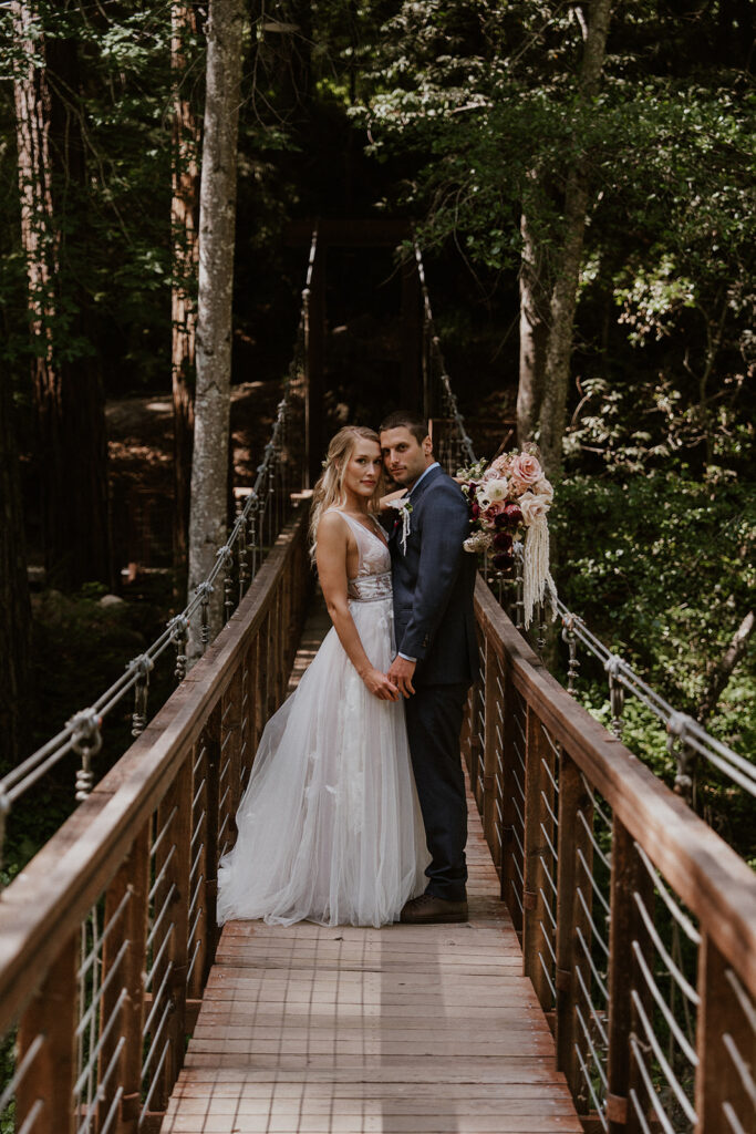 Bride and groom posing on an outdoor bridge for their Big Sur redwood elopement photos