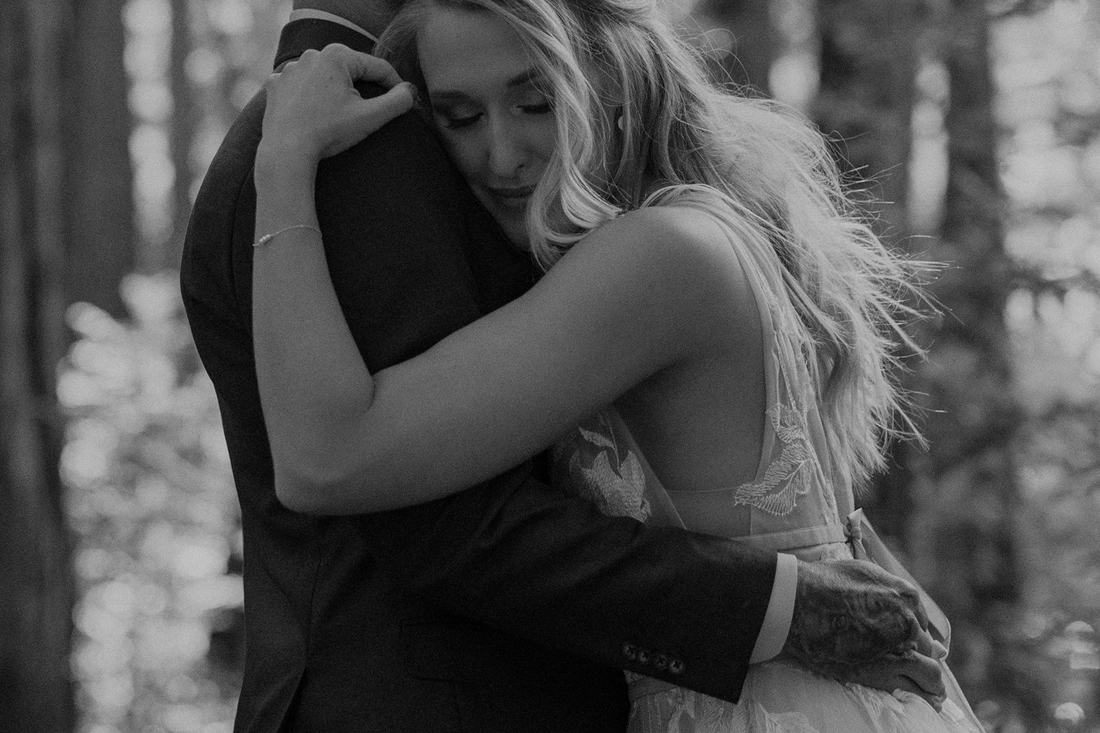 Black and white photo of a bride and groom hugging each other in the redwoods