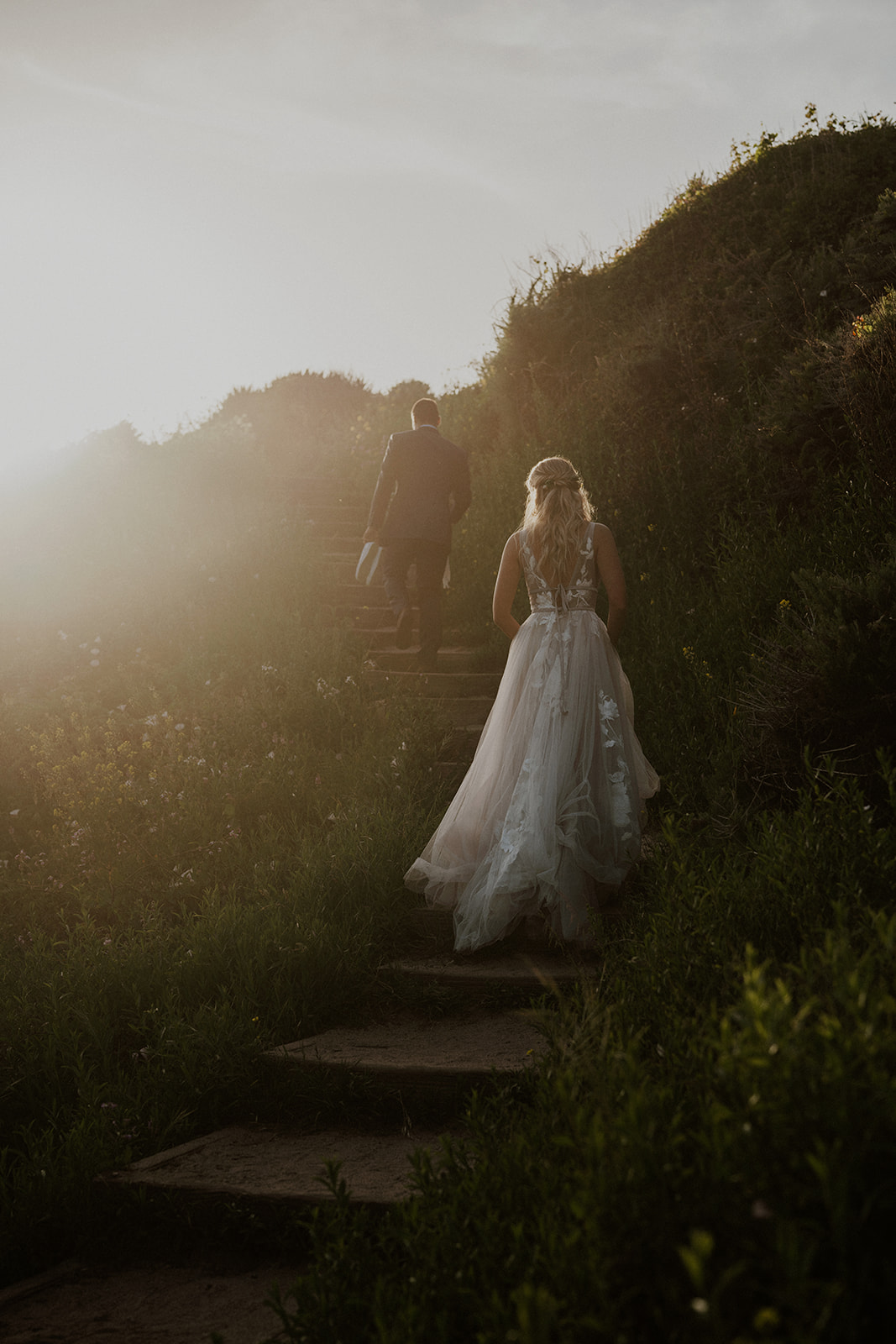 Bride and groom walking about beach stairs at sunset