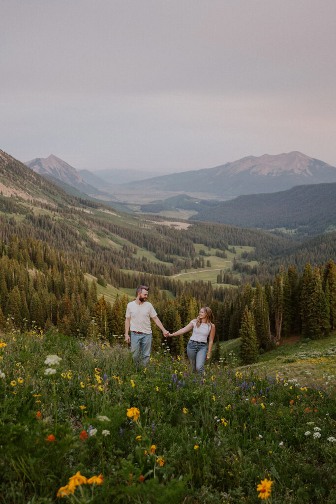 Couple walking hand in hand through wildflowers in Crested Butte with mountains in the background