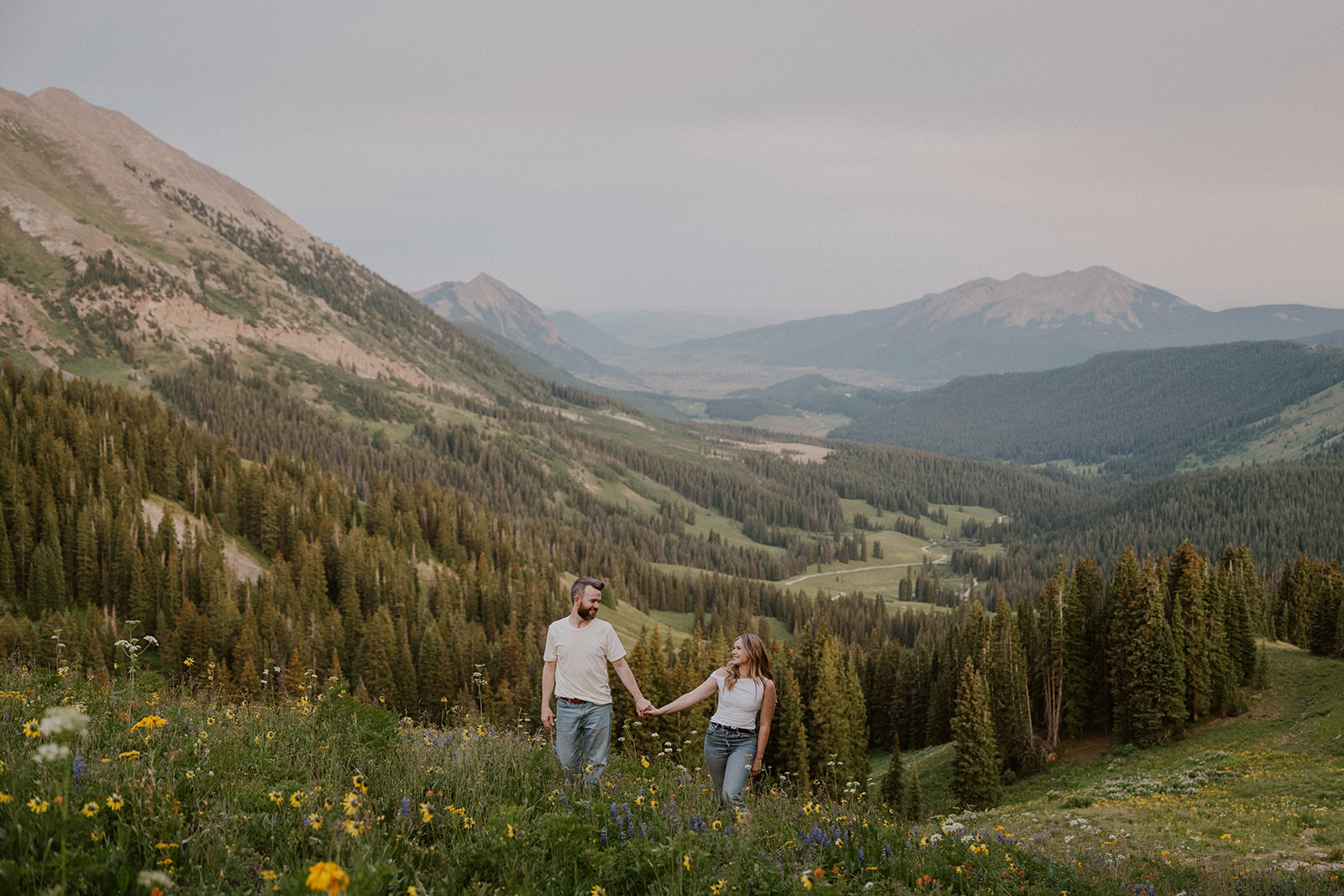 Couple walking up a mountain of wildflowers together in Crested Butte