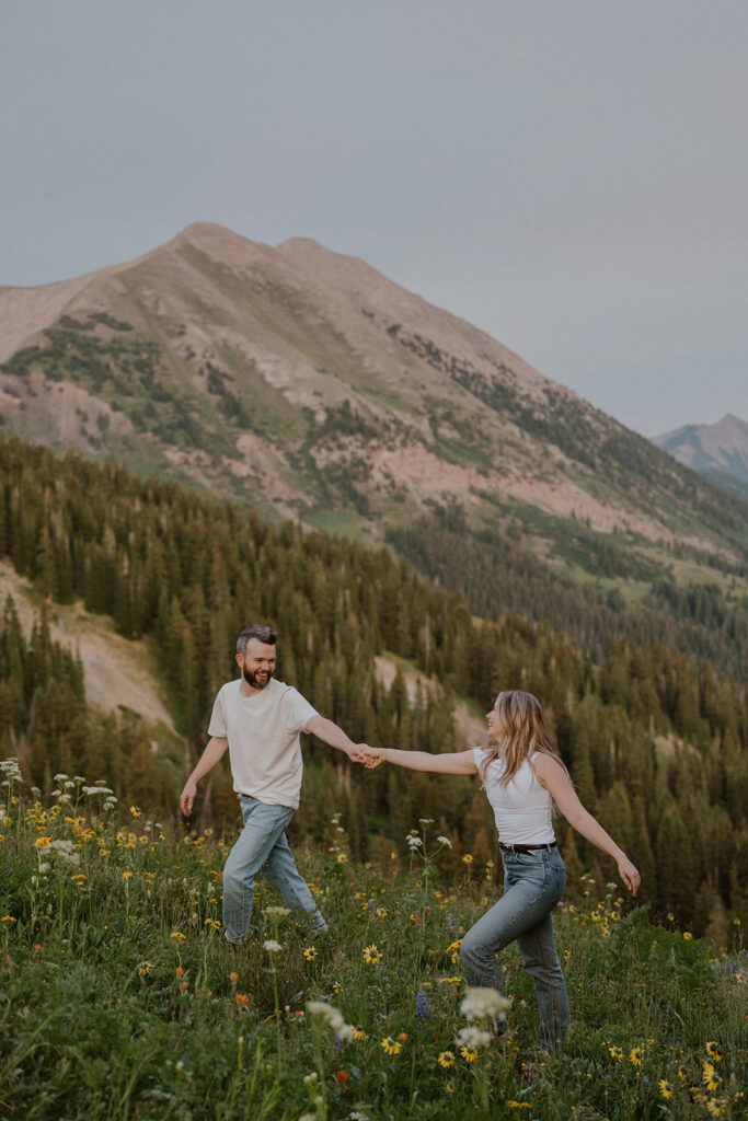 Couple walking up a mountain of wildflowers together in Crested Butte
