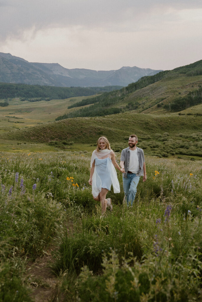 Couple walking side by side through wildflowers, smiling during their Crested Butte engagement photos.