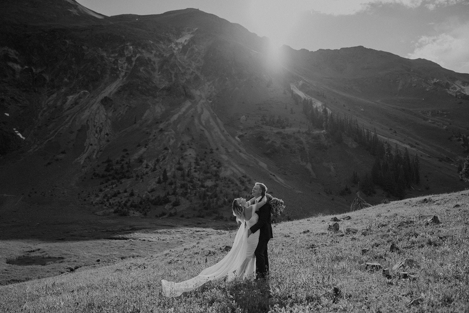 Black and white photo of a bride and groom laughing in the mountains