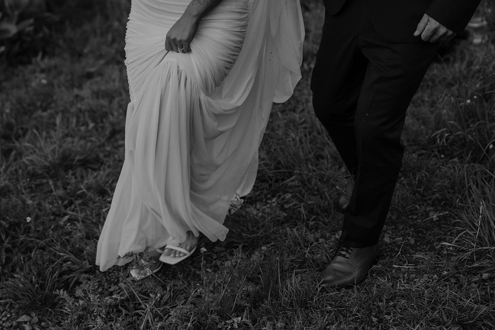Black and white close up shot of a bride and groom walking in the mountains