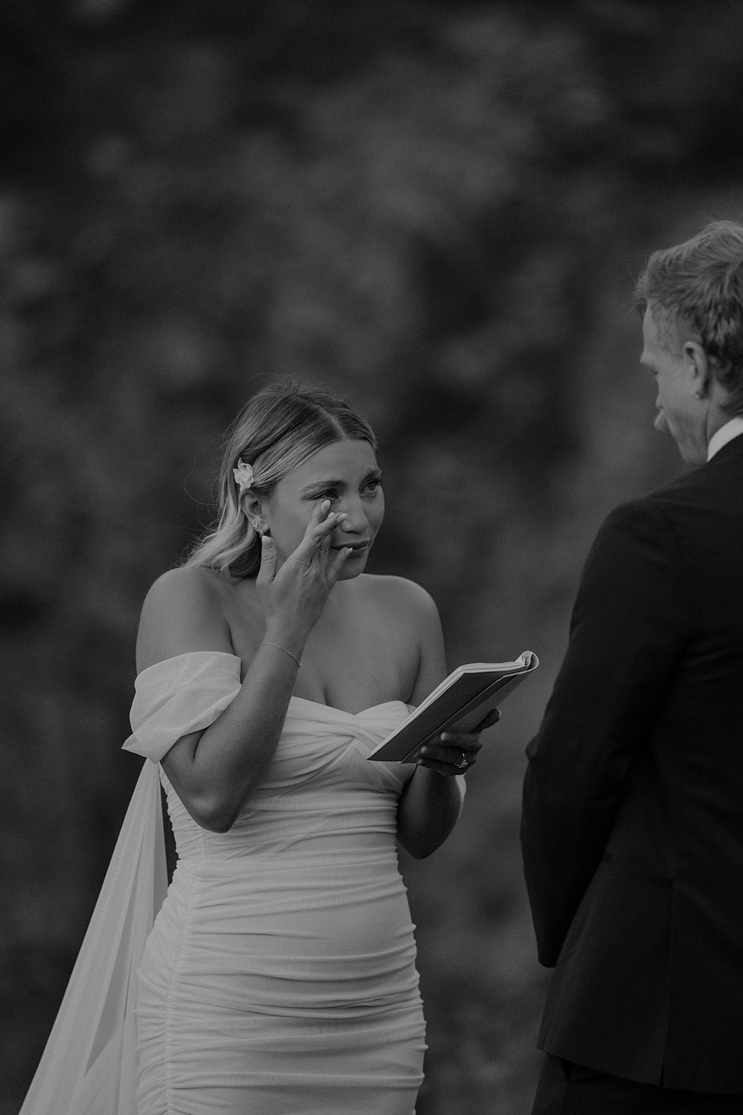 Black and white photo of a bride getting emotional during their vow exchange in the mountains