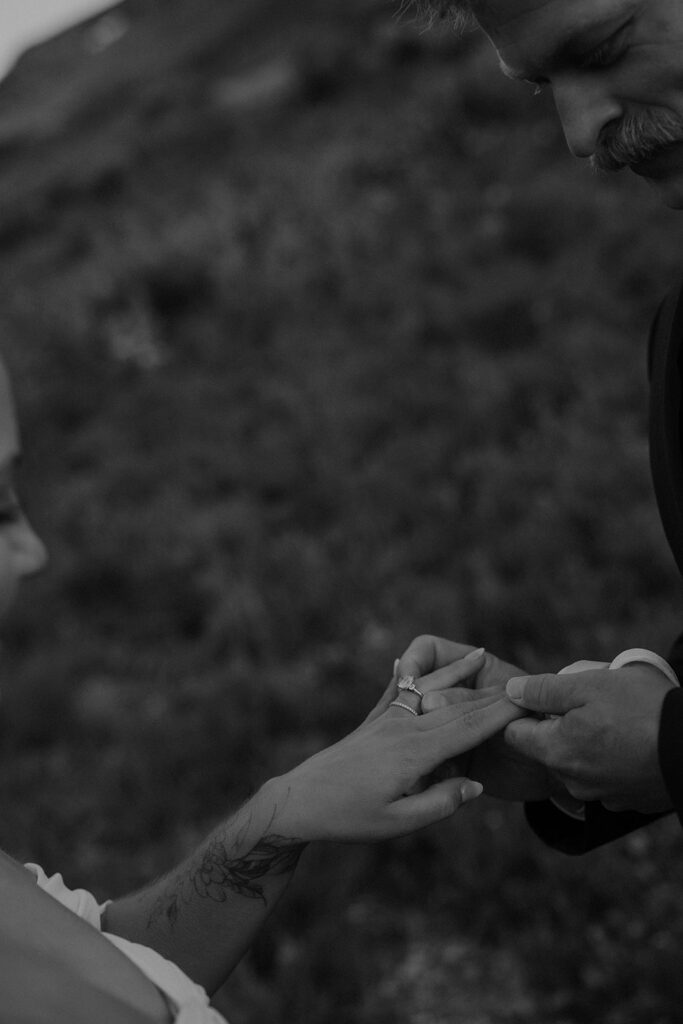 Black and white photo of a groom placing the ring on his brides finger