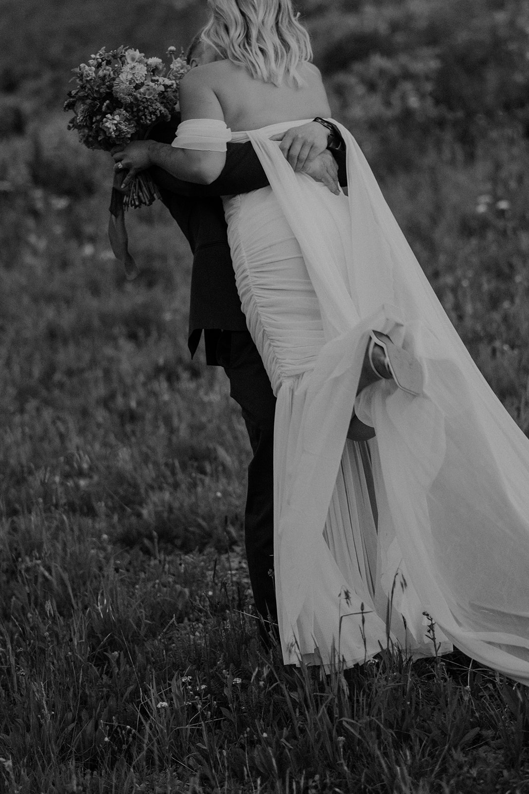 Close up black and white photo of a groom lifting his bride in the air