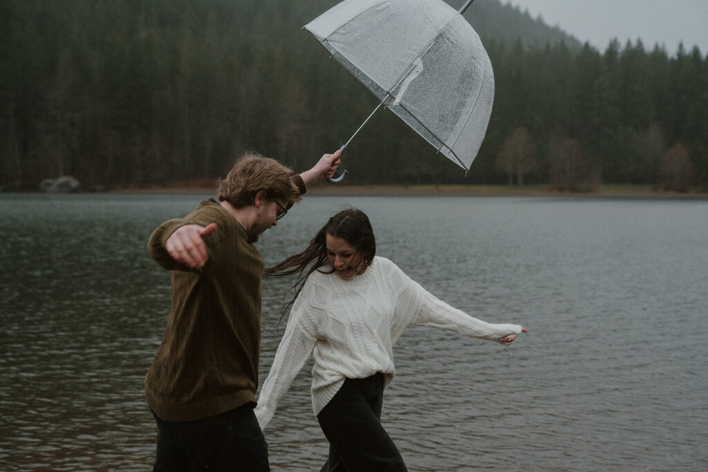 Playful lake engagement photos in Washington State with clear umbrellas