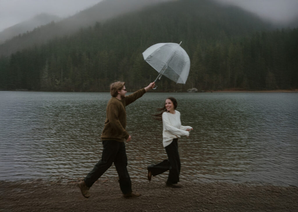 Playful lake engagement photos in Washington State with clear umbrellas