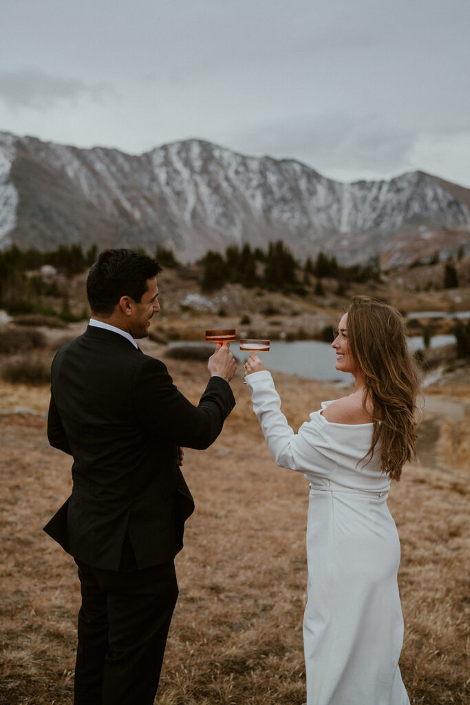 Bride and groom drink champagne by an alpine lake on Loveland Pass