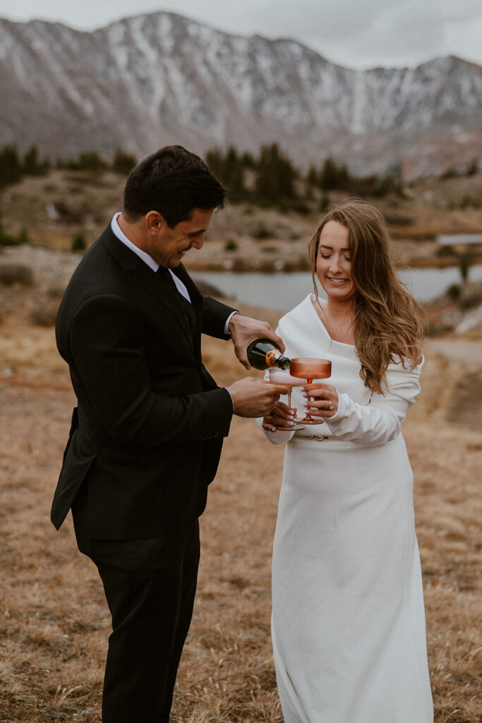 Bride and groom drink champagne by an alpine lake on Loveland Pass