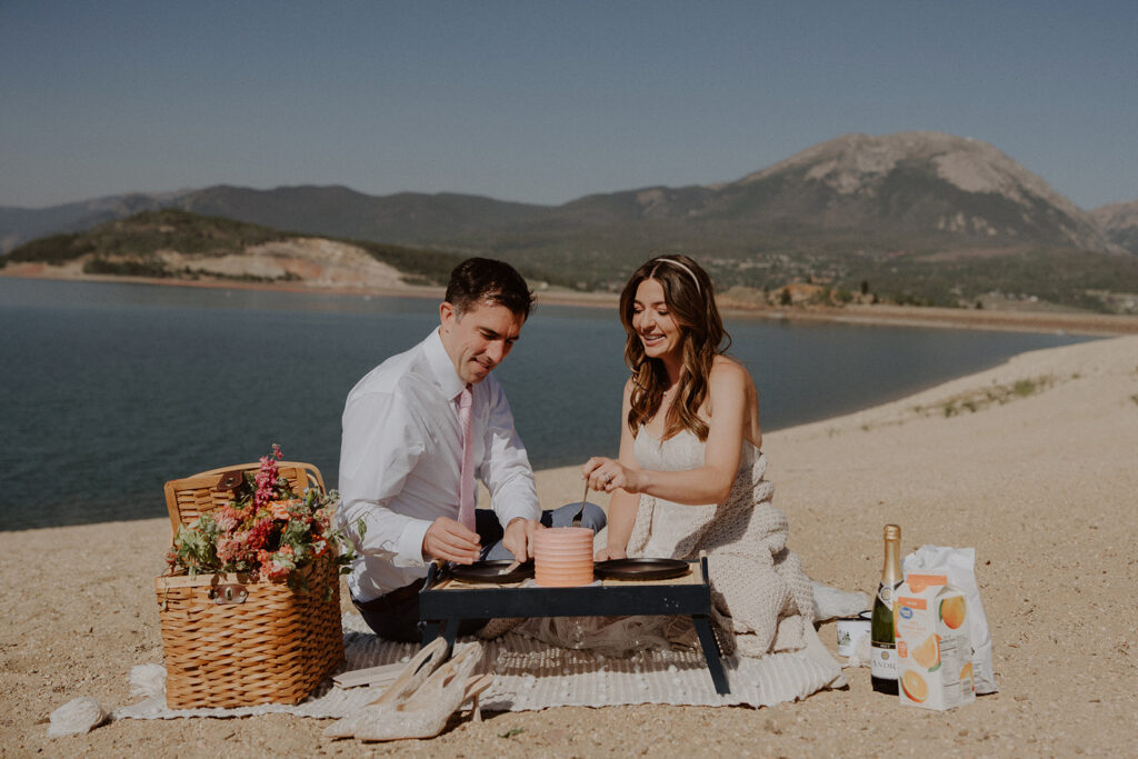 Bride and groom have cake and drinks on a lakeside in Colorado