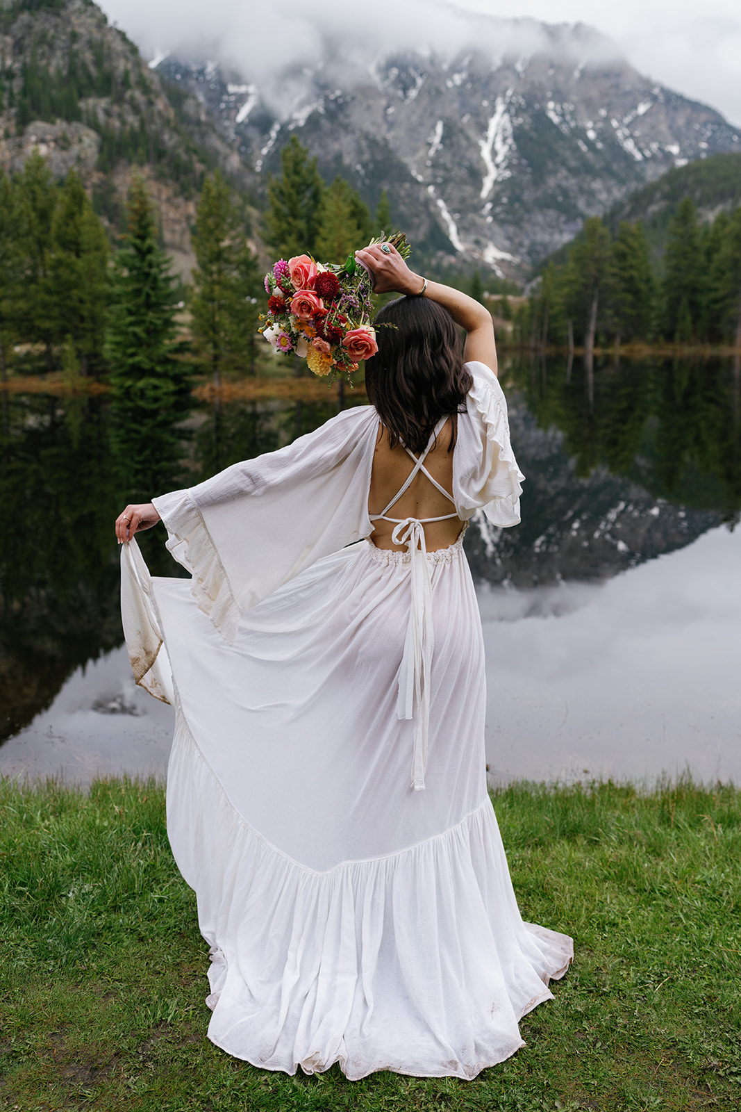 A bride twirls and plays with her dress while standing on the edge of a mountain lake Blue lakes Breckenridge Elopement