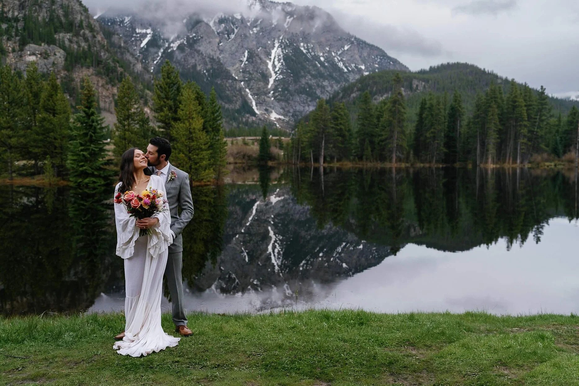 Newlyweds kiss by a lake in front of snowy mountains surf hotel wedding