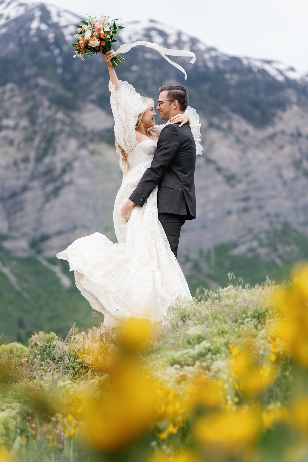Newlyweds celebrate while standing in a field of wildflowers in the mountains