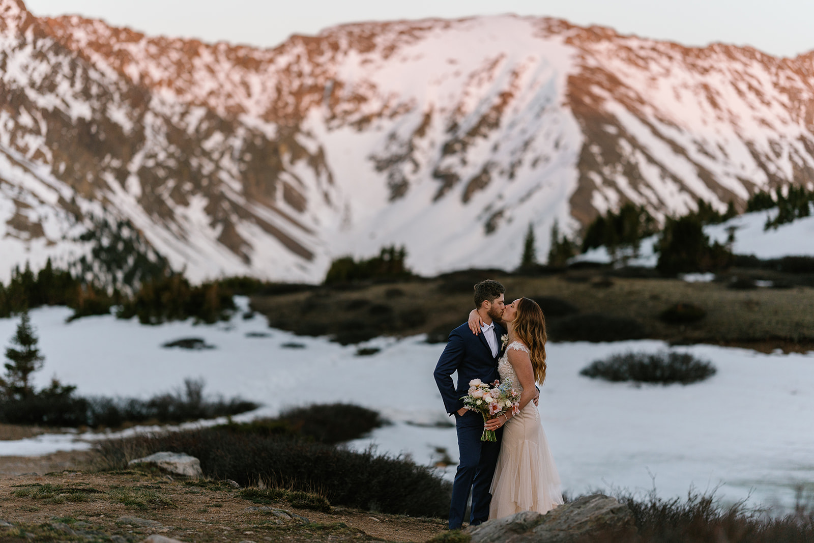 Newlyweds kiss on a mountain trail in front of snow-covered valley and mountains Cheyenne Mountain State Park Wedding