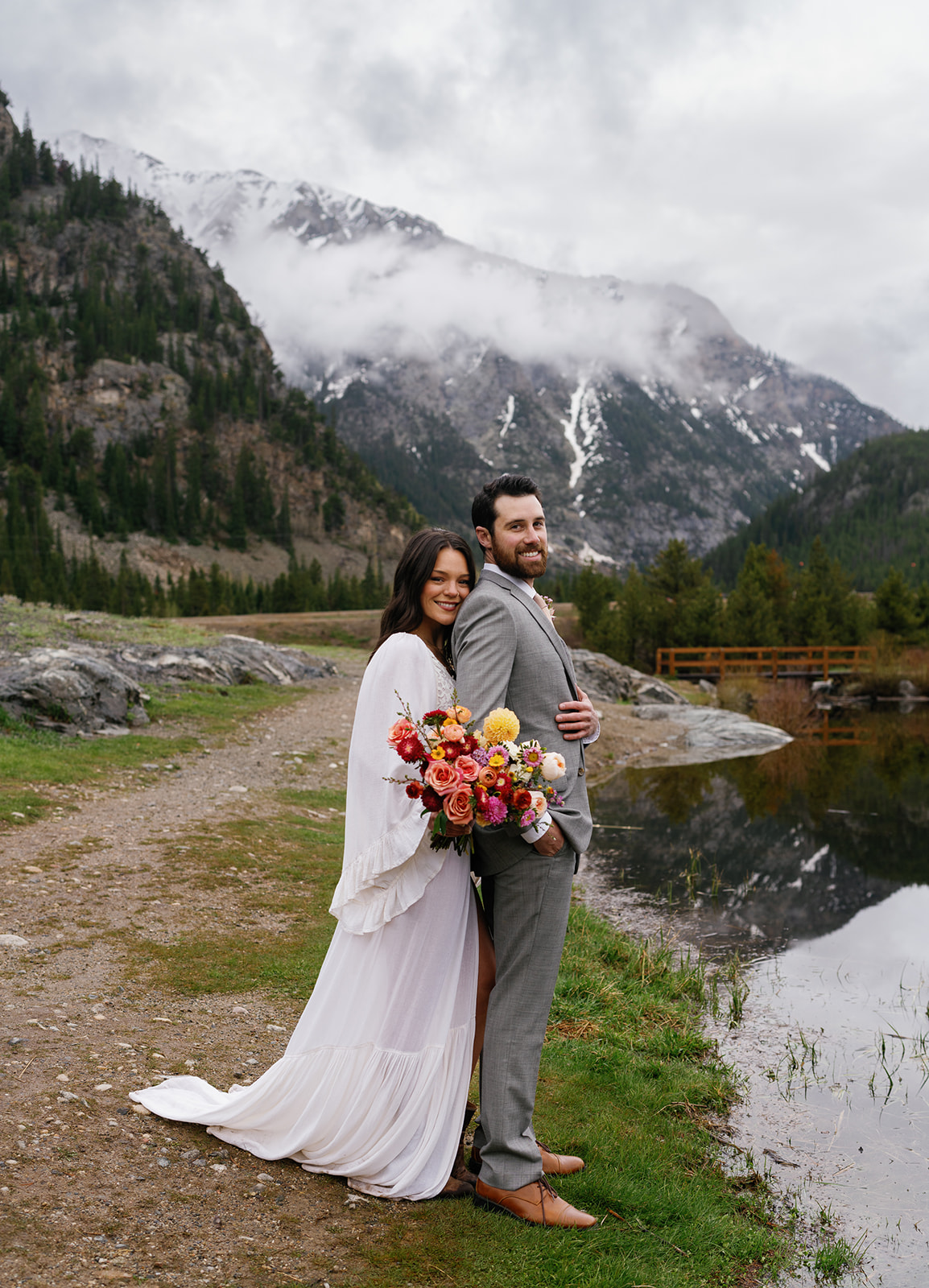 Newlyweds stand on the edge of a mountain lake hugging devils thumb ranch wedding