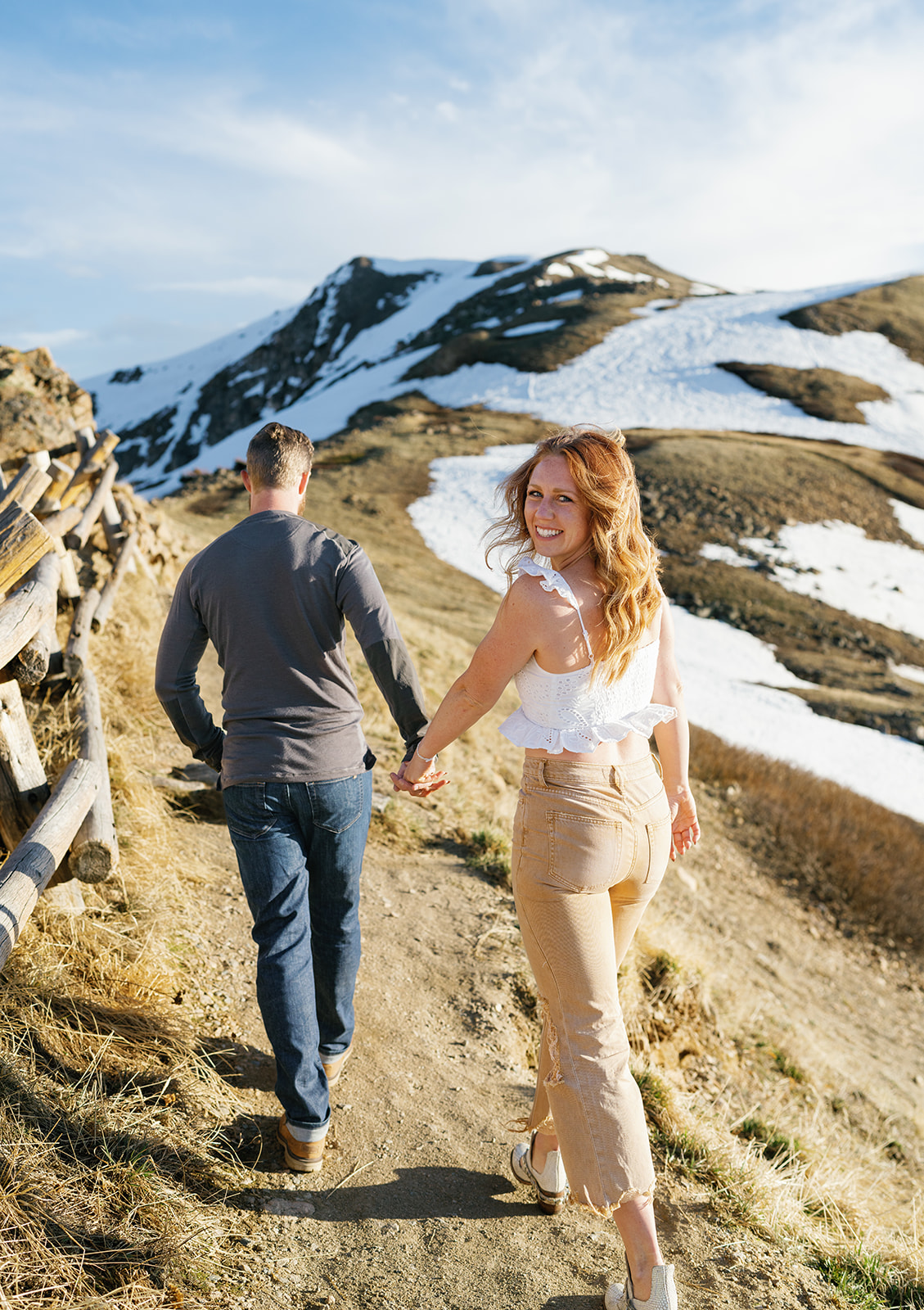 A woman in a white top and khaki pants looks over her shoulder while being led up a snowy mountain trail Roxborough State Park Wedding