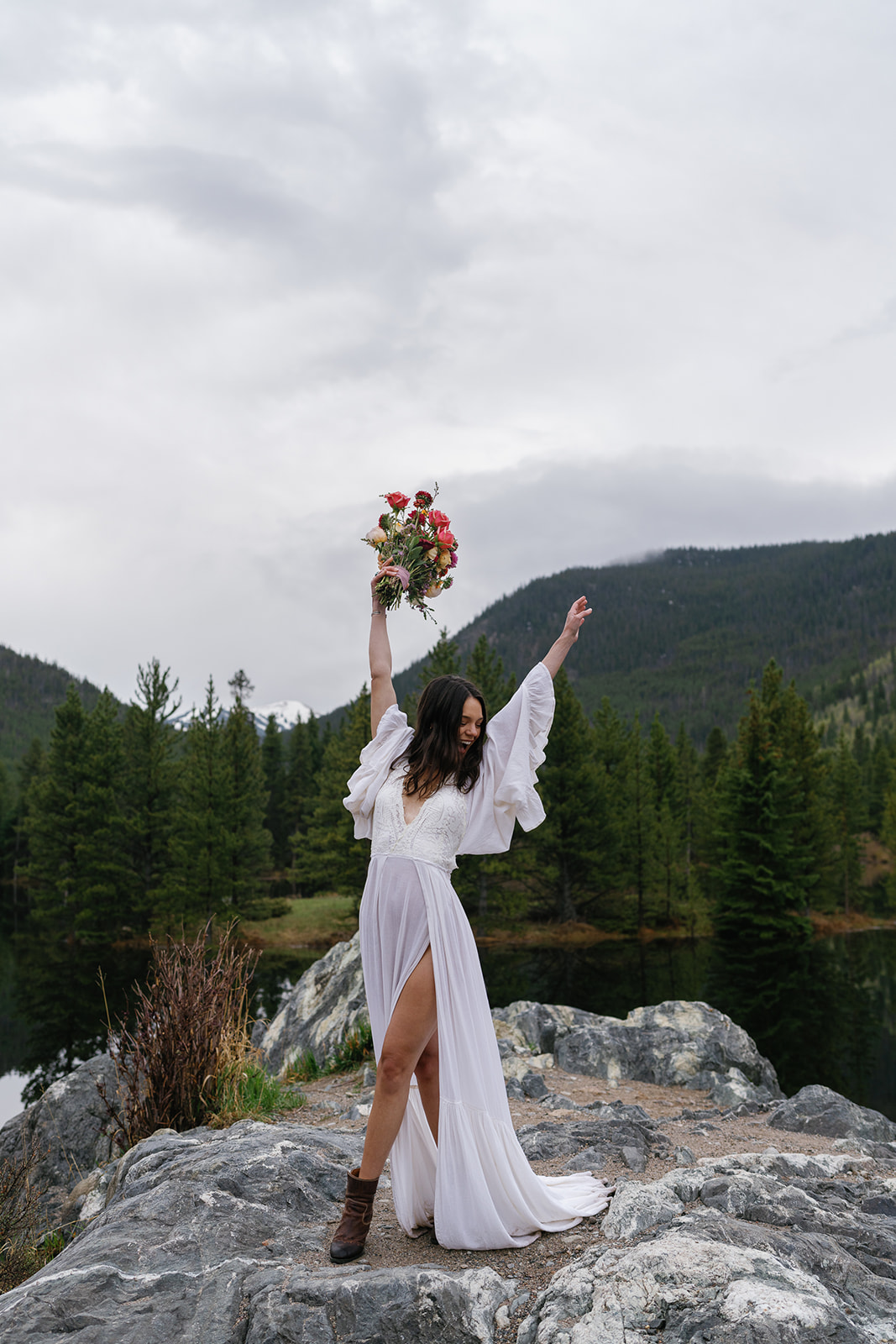 A new bride dances and celebrates while standing on a rock by a lake