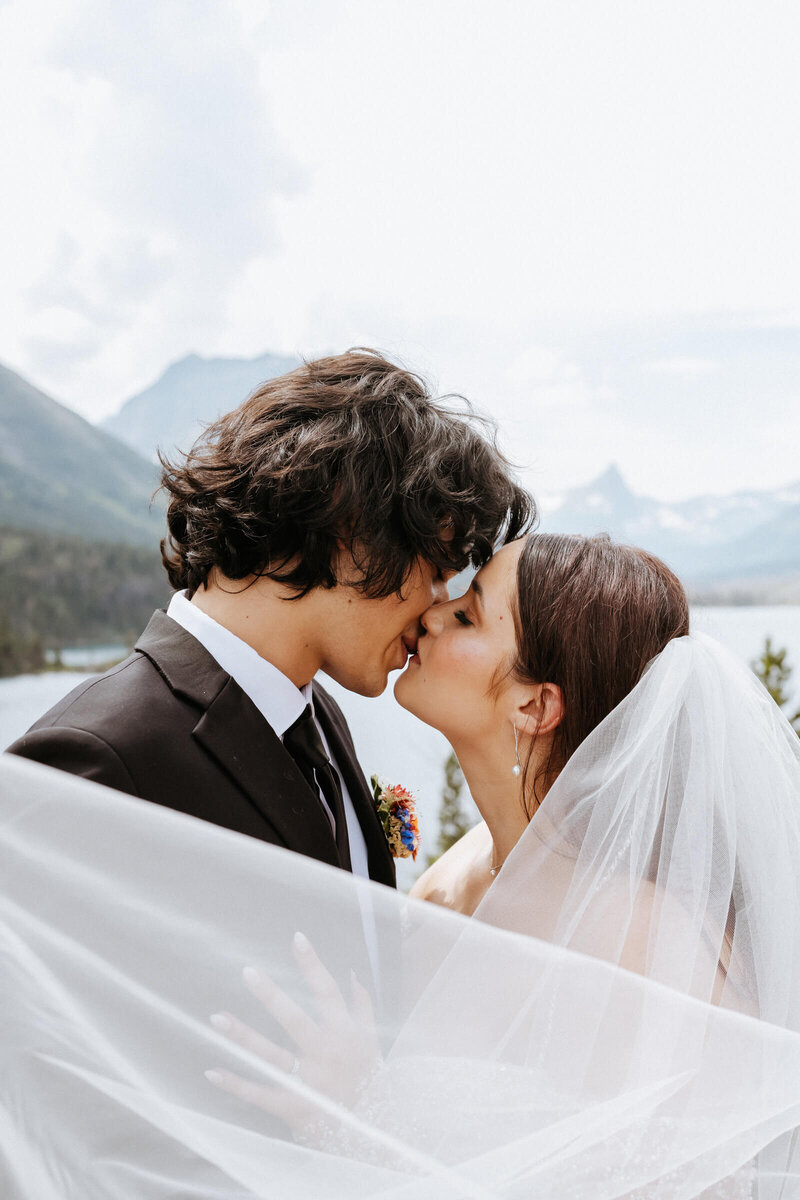 Newlyweds kiss wrapped in the bride's veil in the mountains at Piney River Ranch Wedding