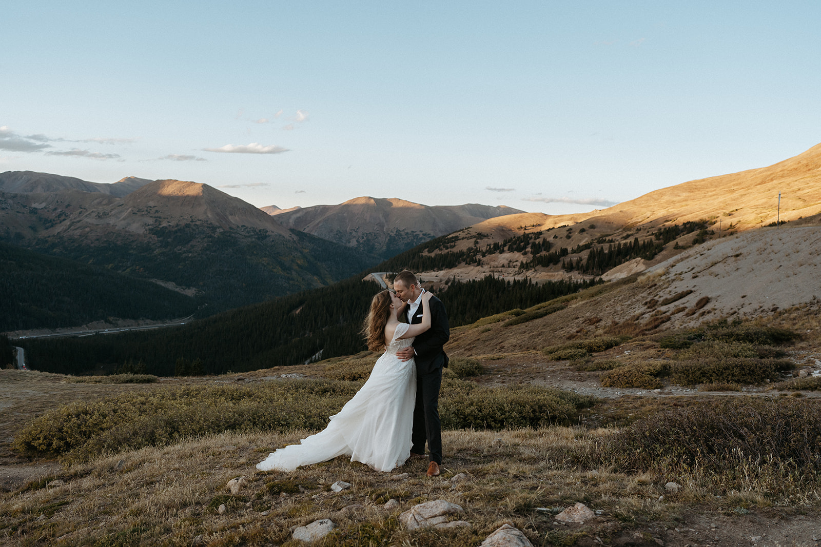 Newlyweds kiss on a mountainside at sunset