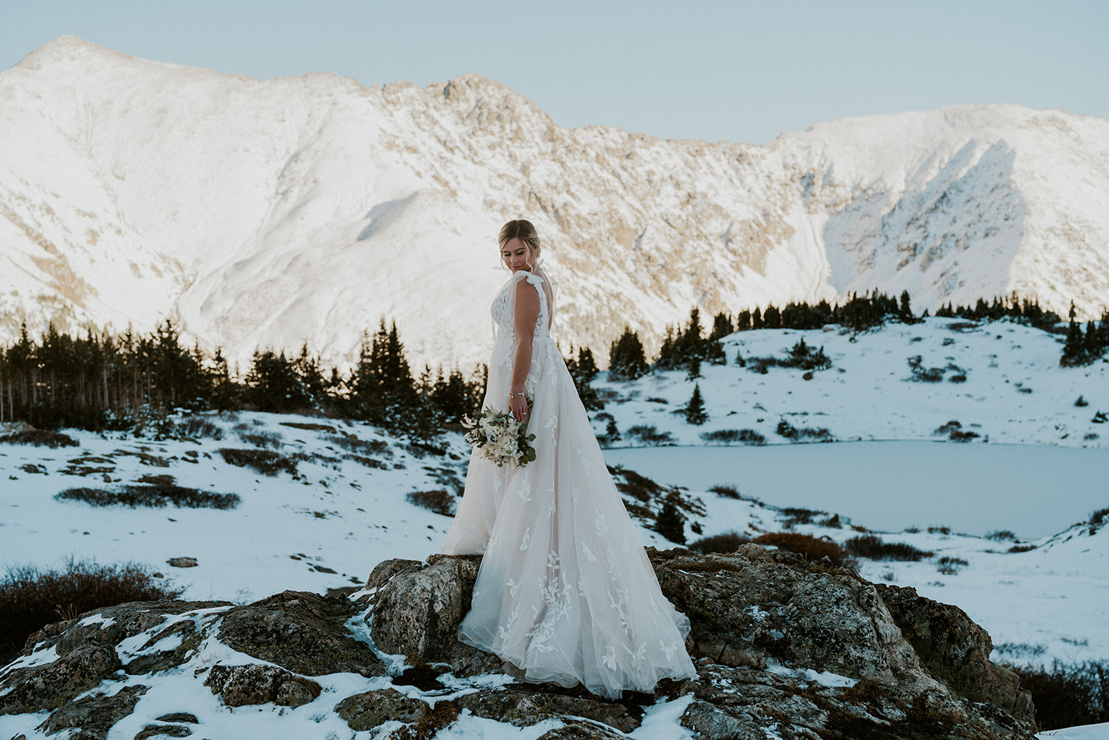 A bride looks down her shoulder while standing on a large rock in Loveland pass during her elopement