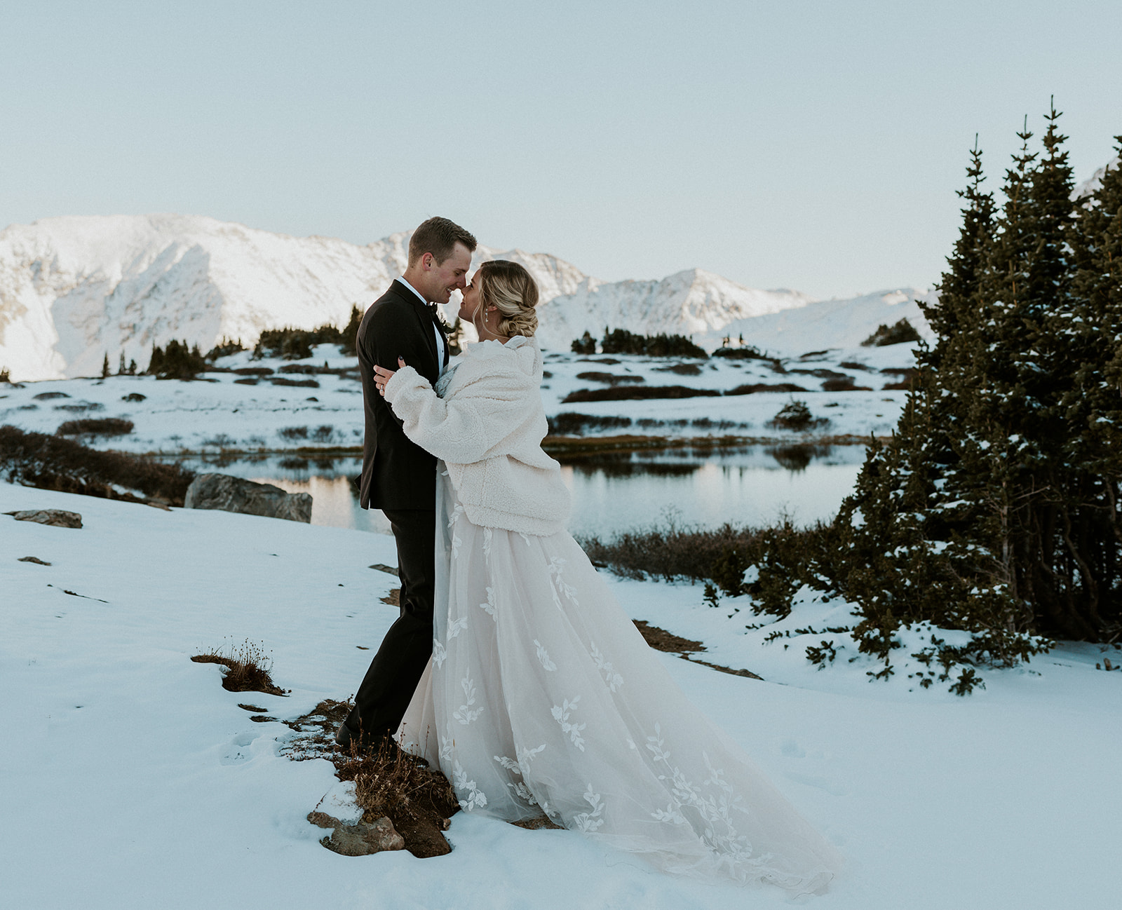 Newlyweds stand nose to nose in the snow by a lake during their Loveland Pass Elopement