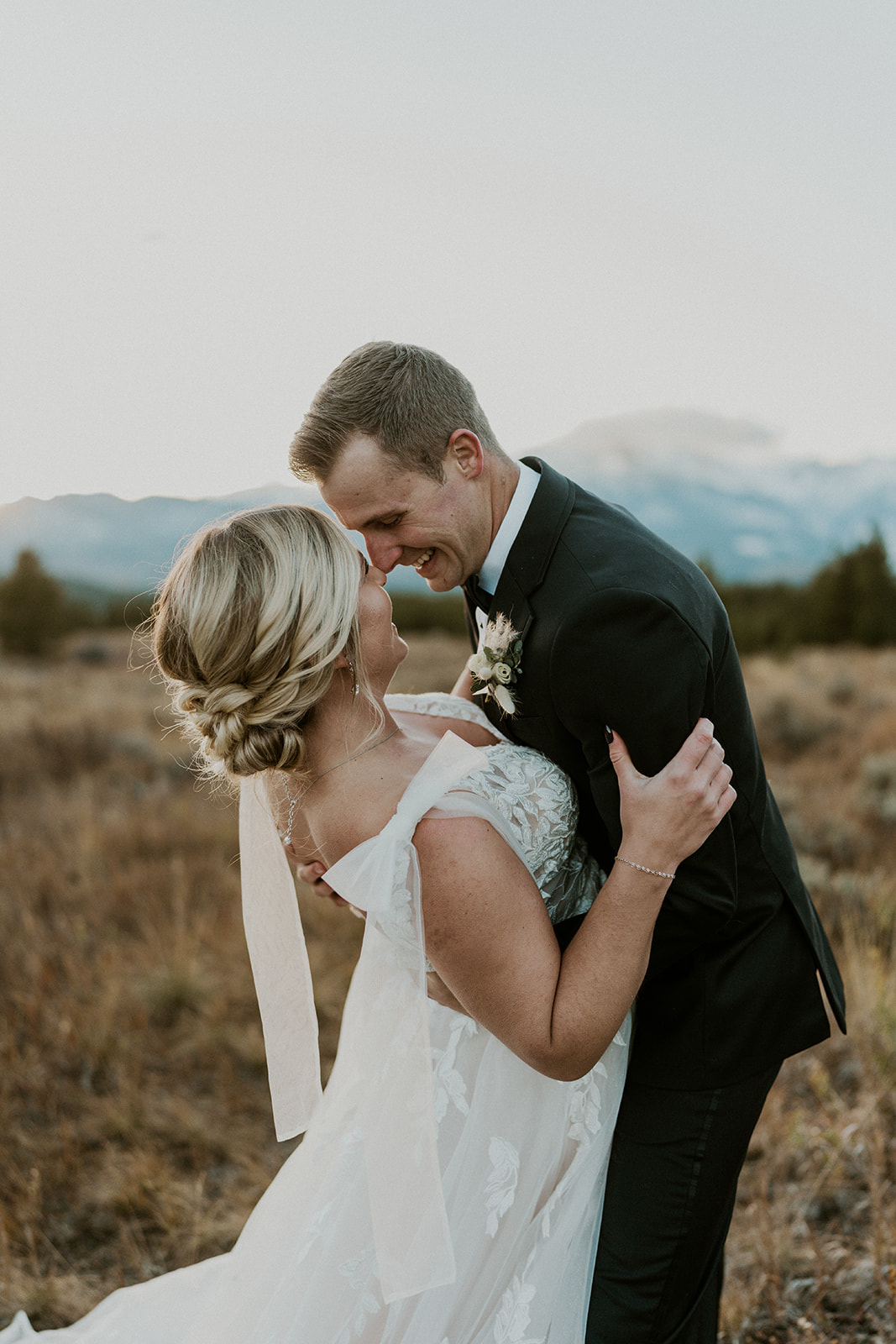 A groom in a black suit dips his bride in a lace dress at sunset on a mountain trail at their Loveland Pass Elopement