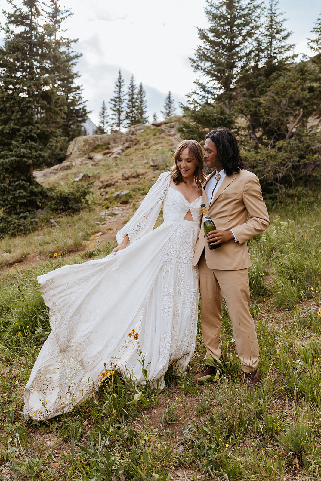 A bride's dress flows in the wind as she stands with her groom in a tan suit laughing