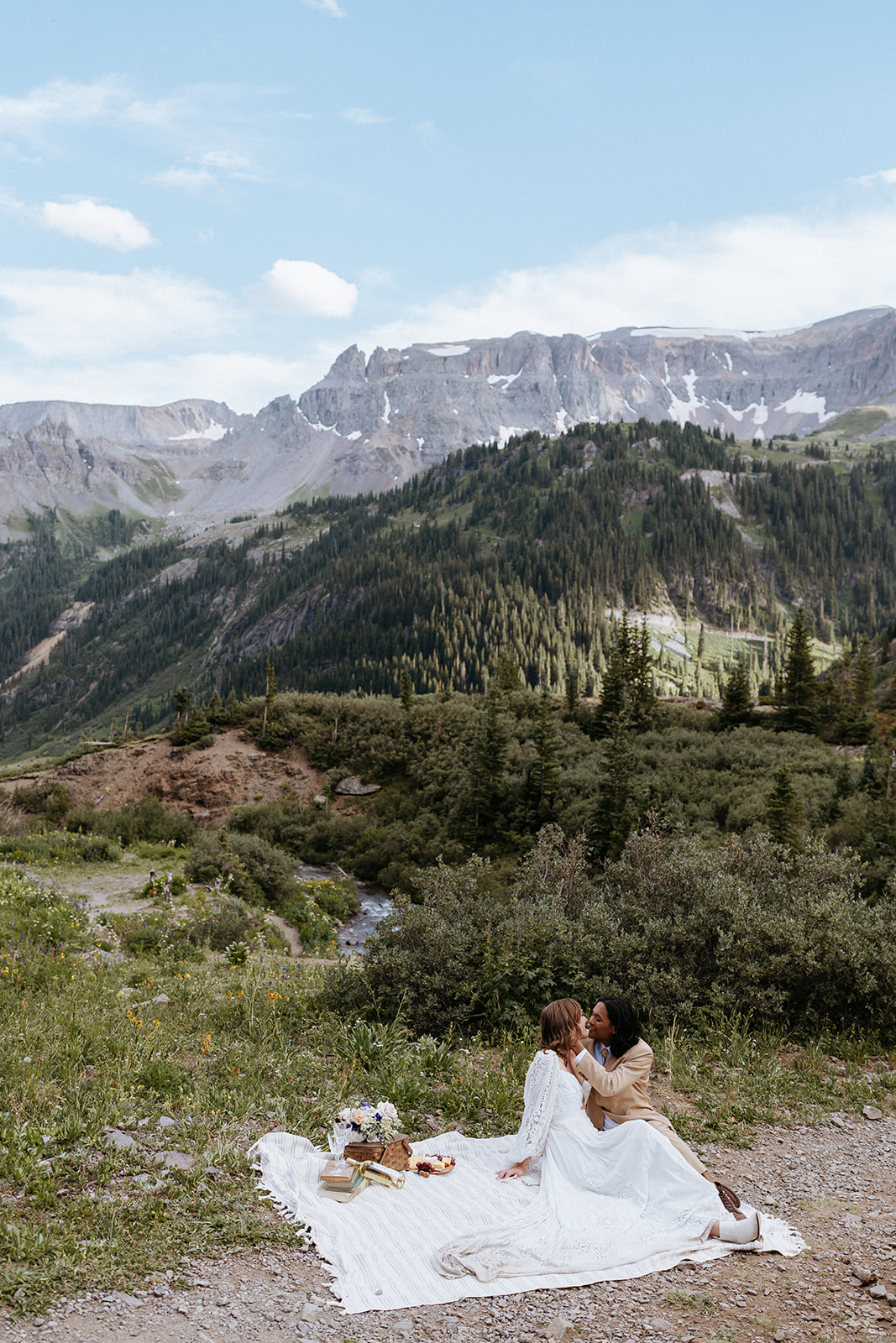 Newlyweds kiss while sitting on a picnic blanket with a picnic set up overlooking Ouray