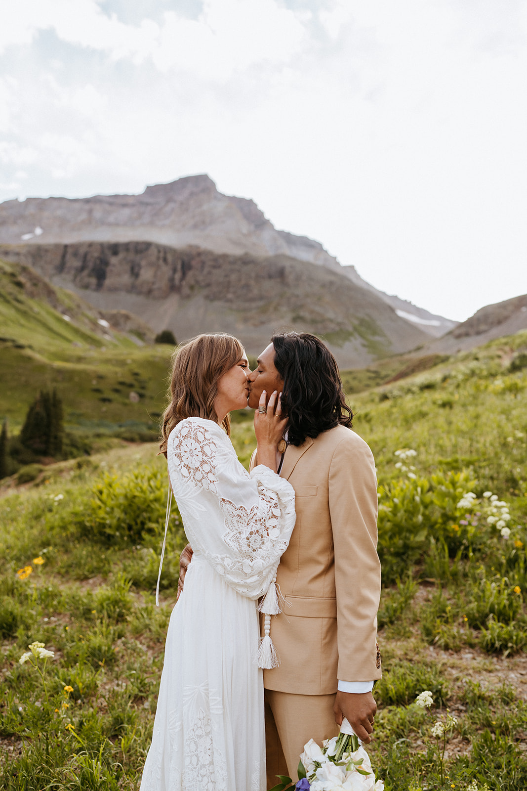 Newlyweds kiss on a mountain trail surrounded by wildflowers during their Ouray Elopement