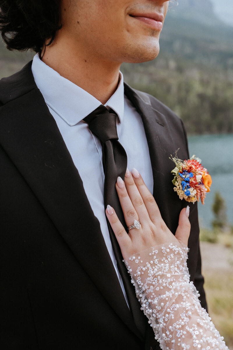 Details of a bride with long lace sleeves resting her hand on her groom's chest in a black suit