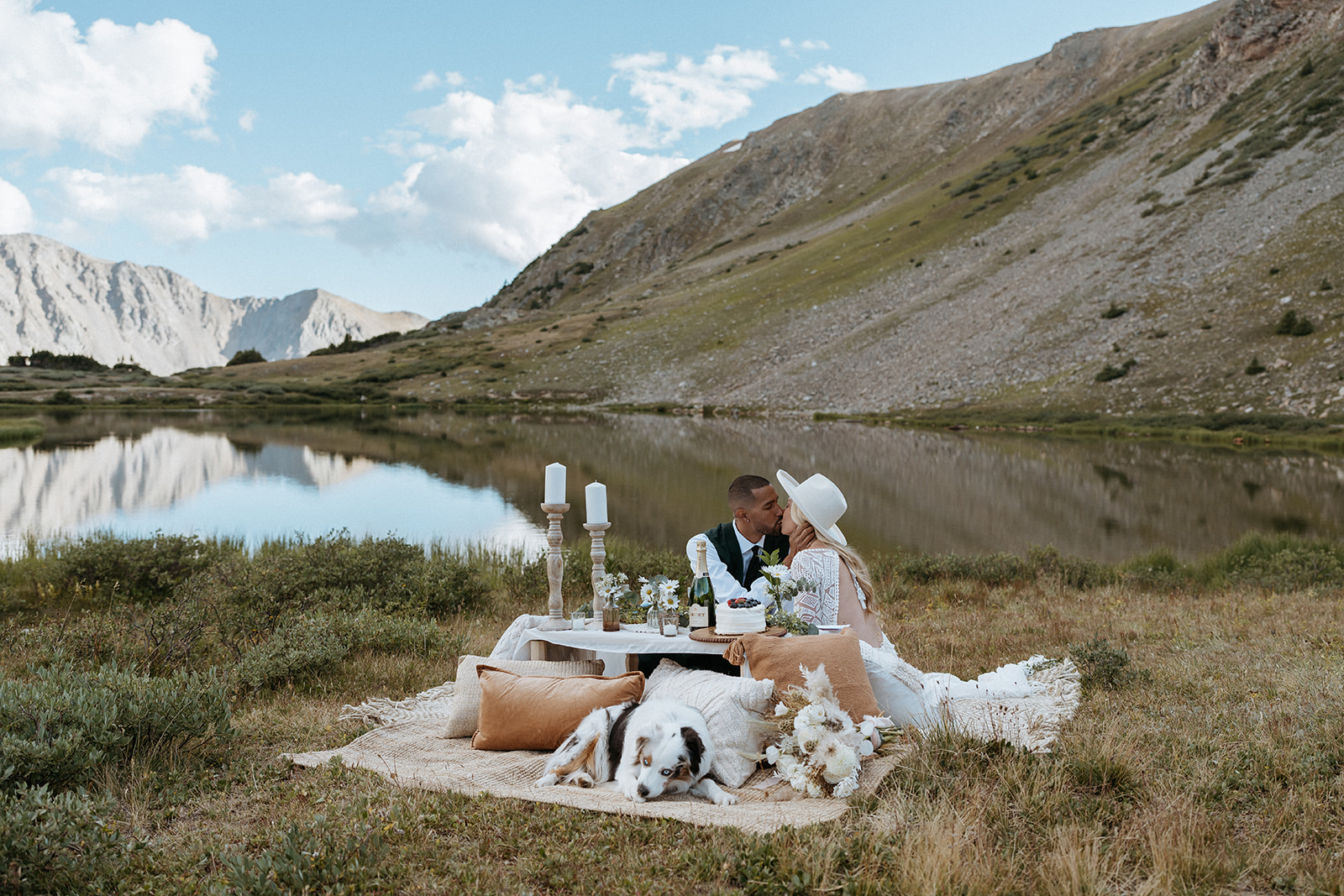 Newlyweds kiss at their elopement picnic table with their dog laying next to them