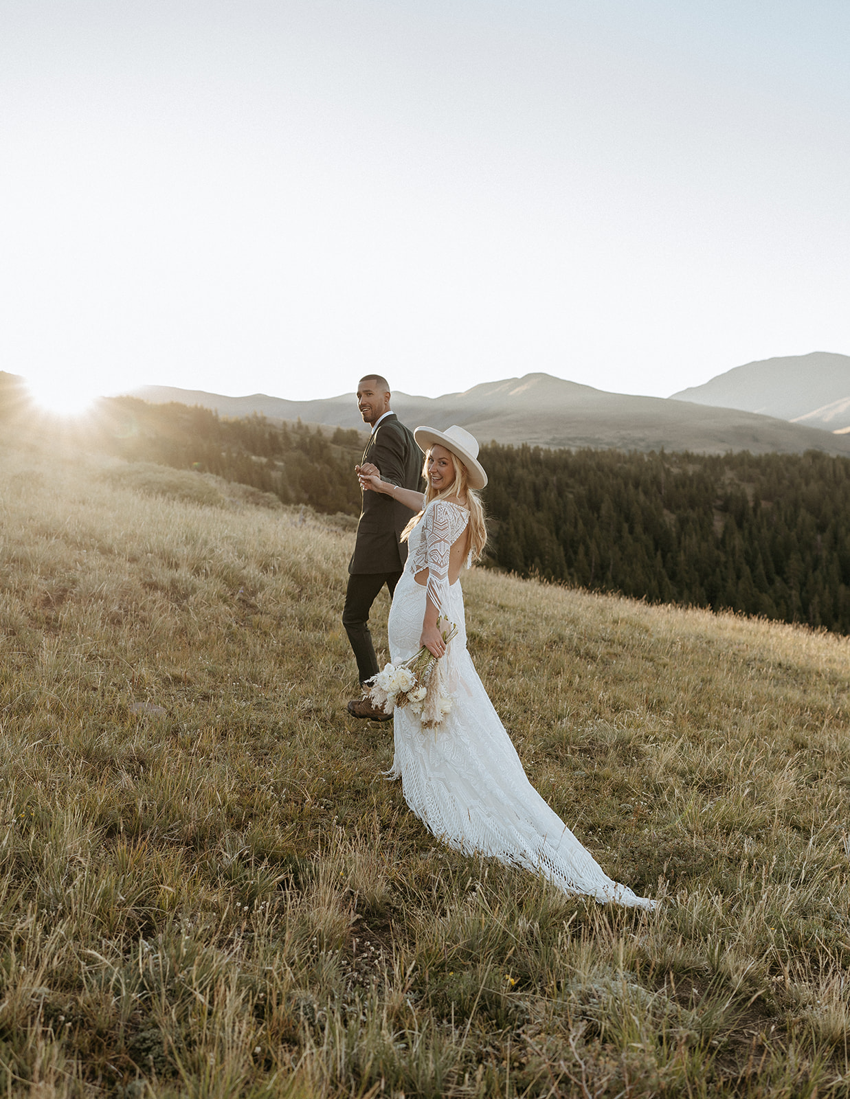 A groom leads his bride up a hillside by the hand into the sunset at their Hoosier Pass Elopement