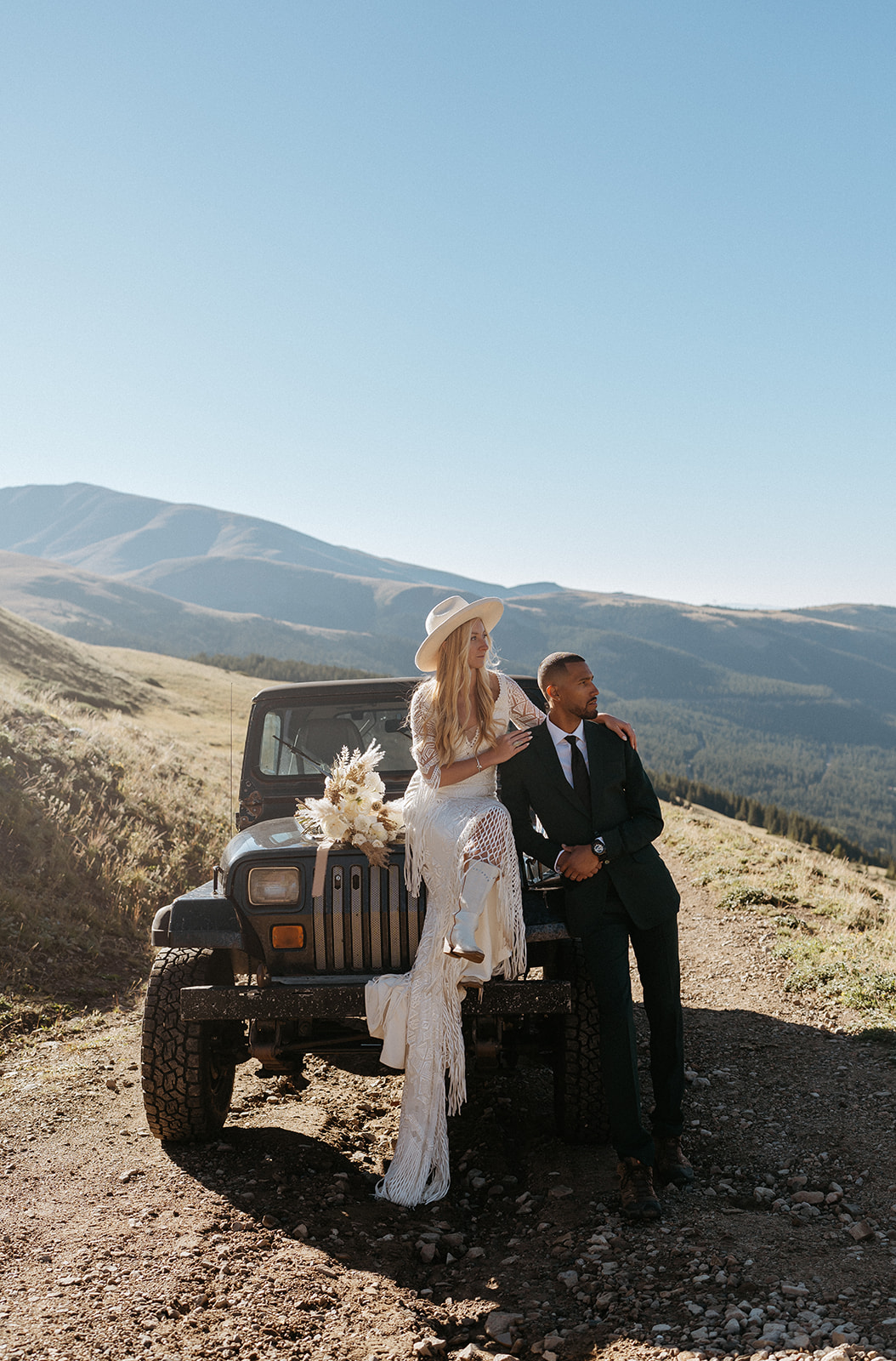 Newlyweds sit and lean on a Jeep on a mountain trail at a Hoosier Pass Elopement