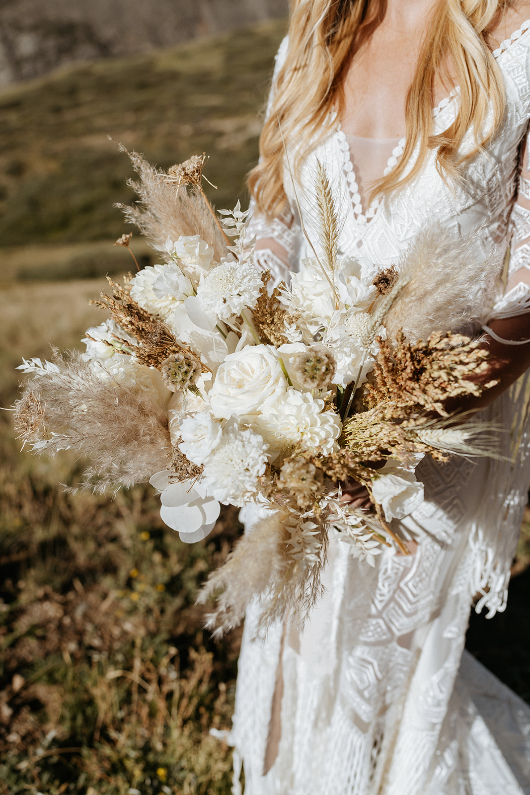 Details of a bride in an embroidered dress holding a boho white rose bouquet