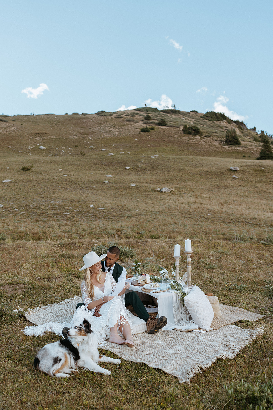 Newlyweds sit on a picnic blanket set up with cake and candles alongside their dog after their Hoosier Pass Elopement