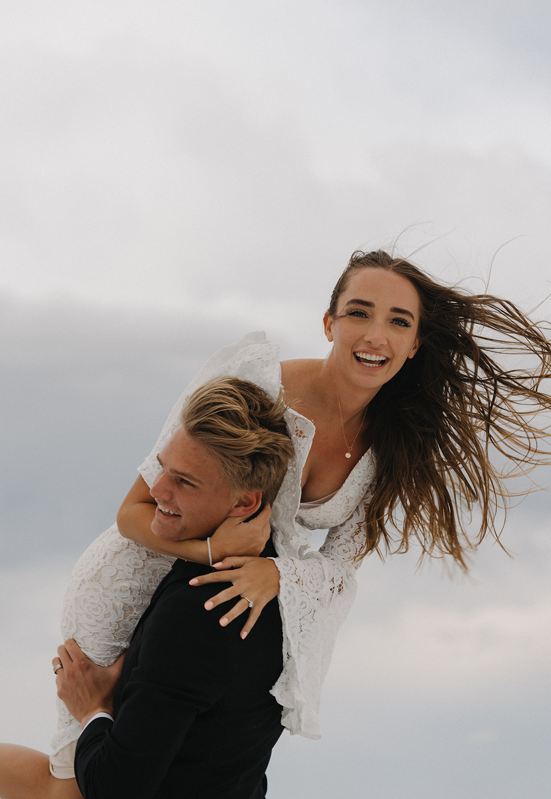 A groom lifts his bride over his shoulder while laughing