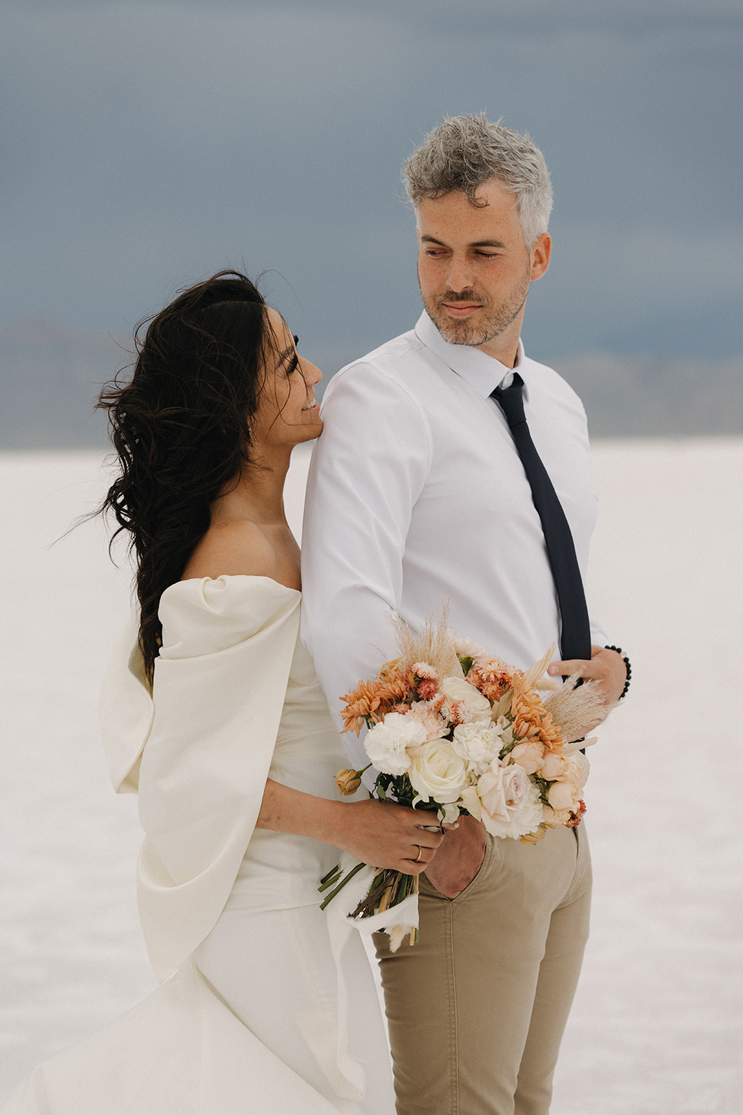 Newlyweds stand together holding each other and a colorful bouquet during their Salt Flats Elopement