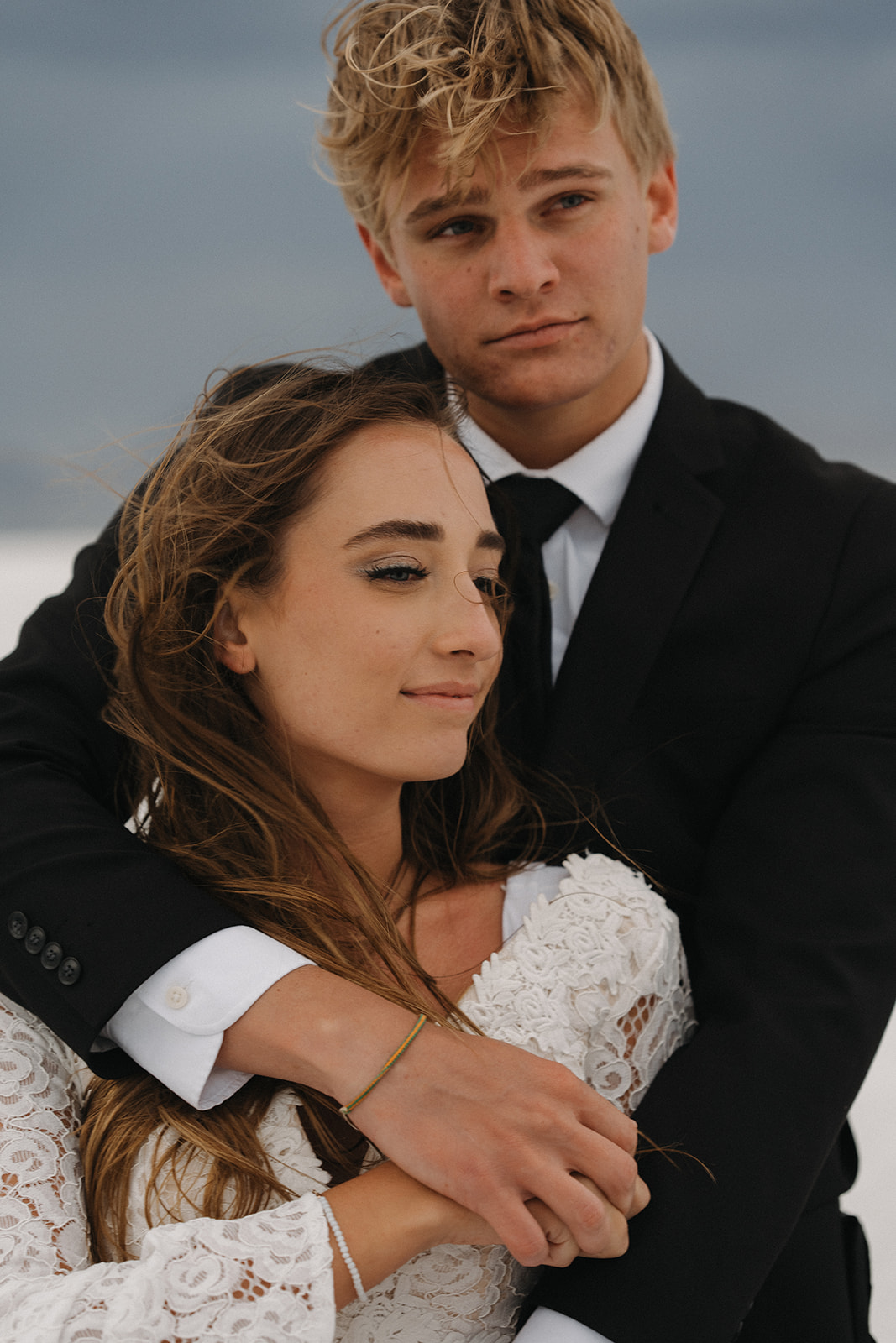Newlyweds stand together hugging and holding hands on a windy day