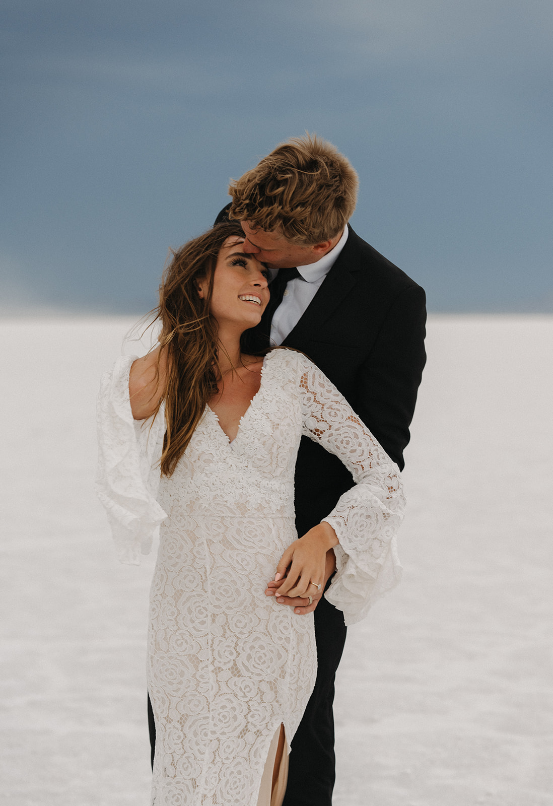 Newlyweds share an intimate moment standing together and kissing the bride's forehead during their Salt Flats Elopement