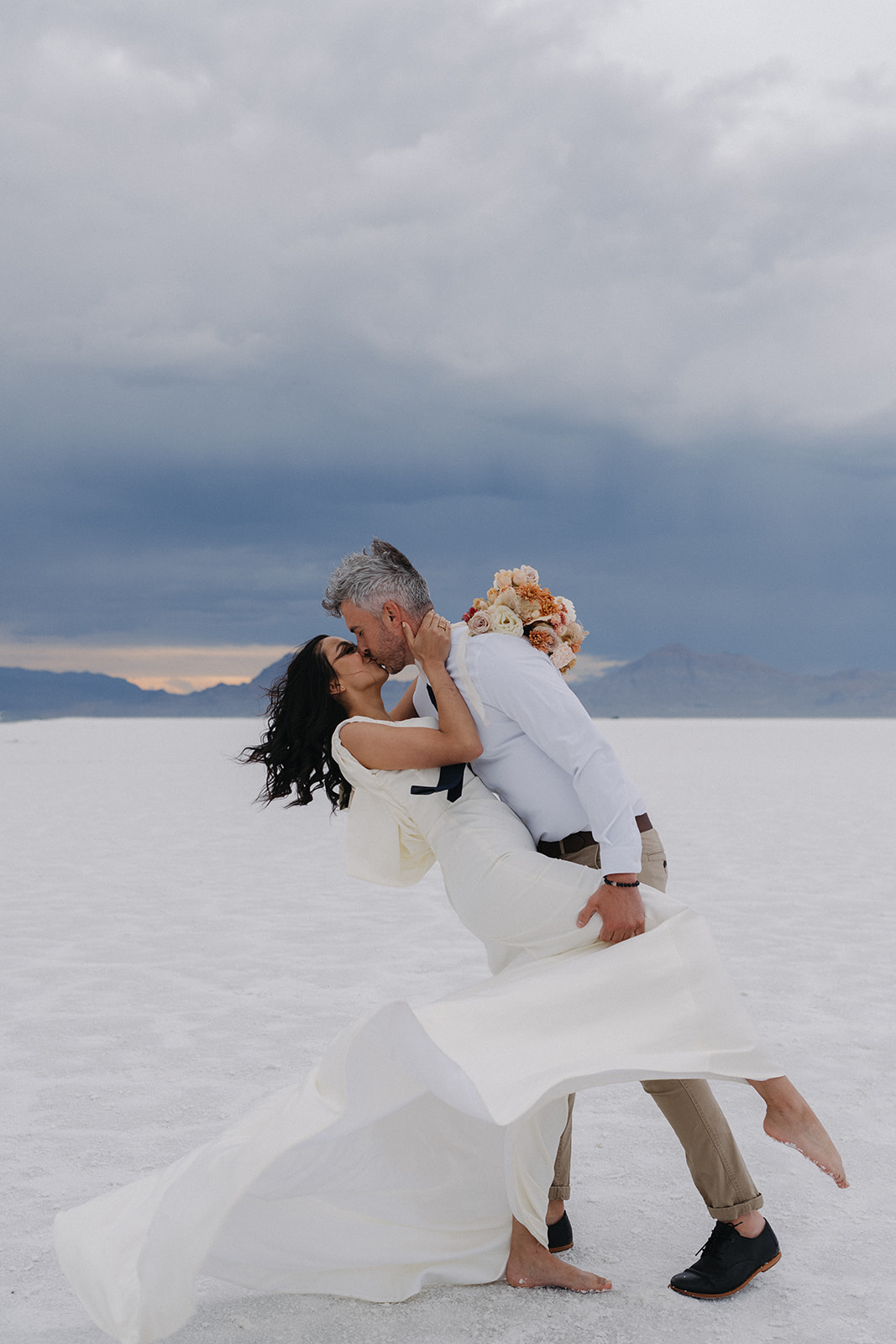 A groom in khakis and white shirt dips his bride for a kiss in the middle of their Salt Flats Elopement