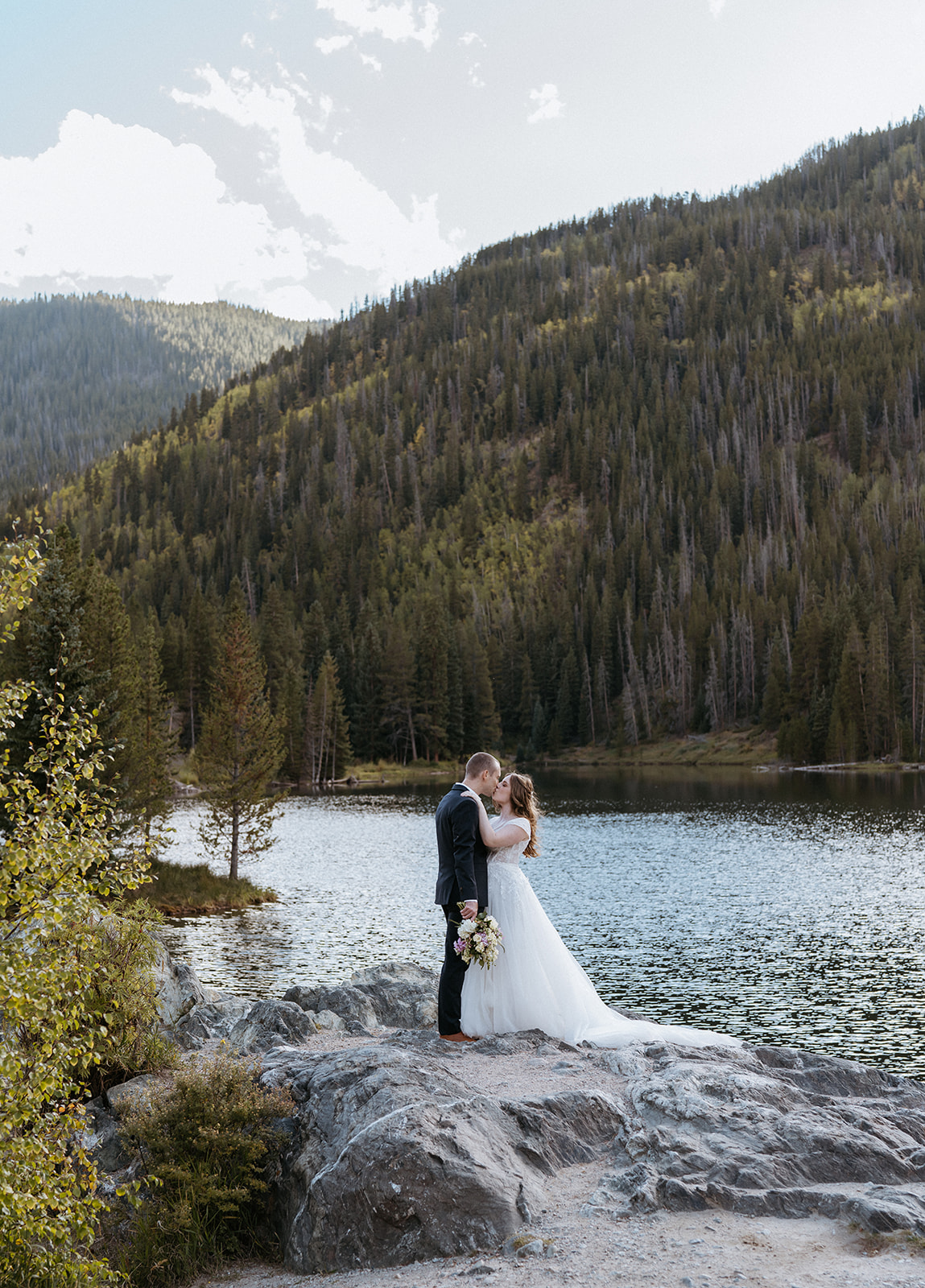 Newlyweds share a kiss on the edge of a rocky mountain lake Colorado Adventure Elopement