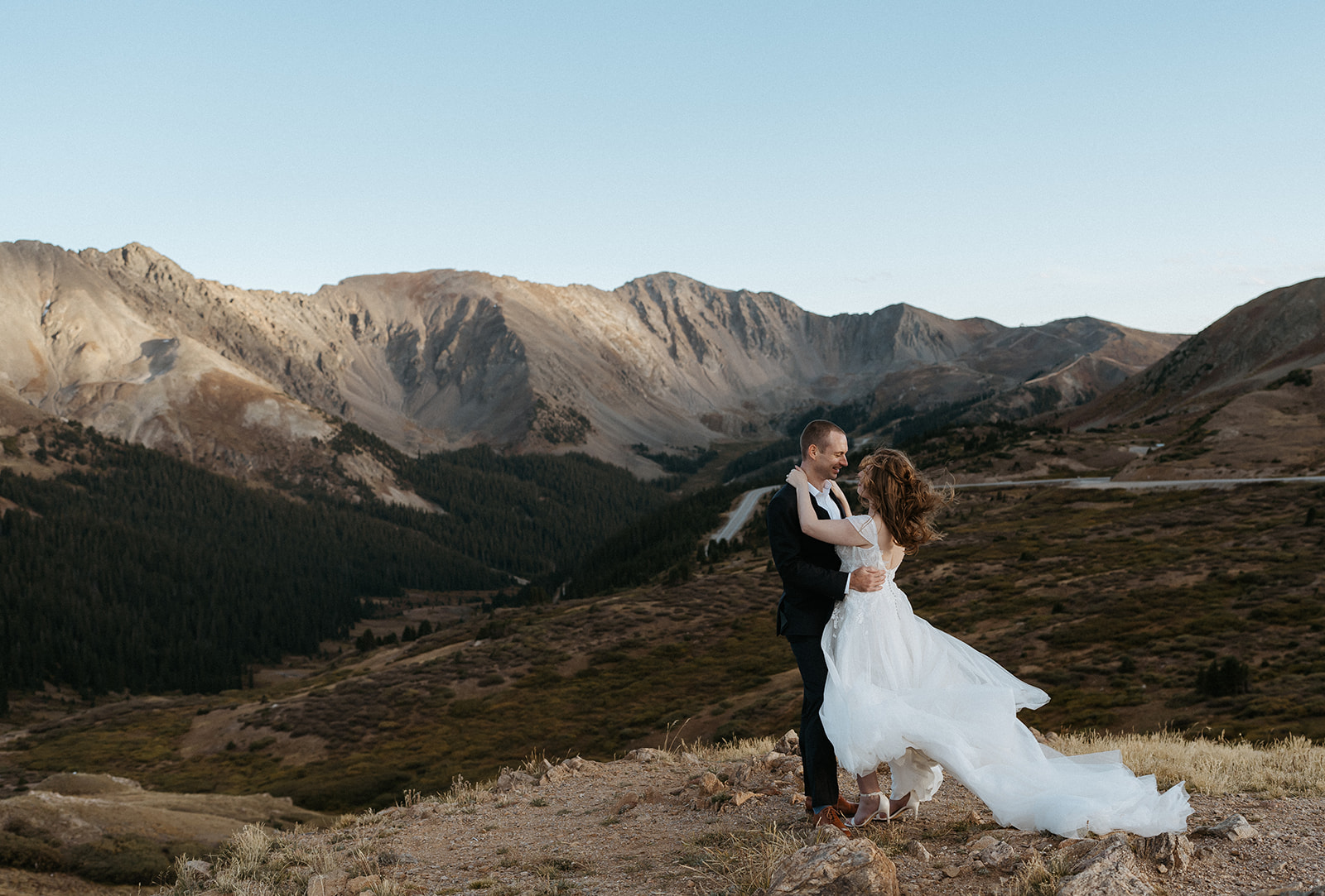 Newlyweds share an intimate moment on a rocky mountainside on a windy day